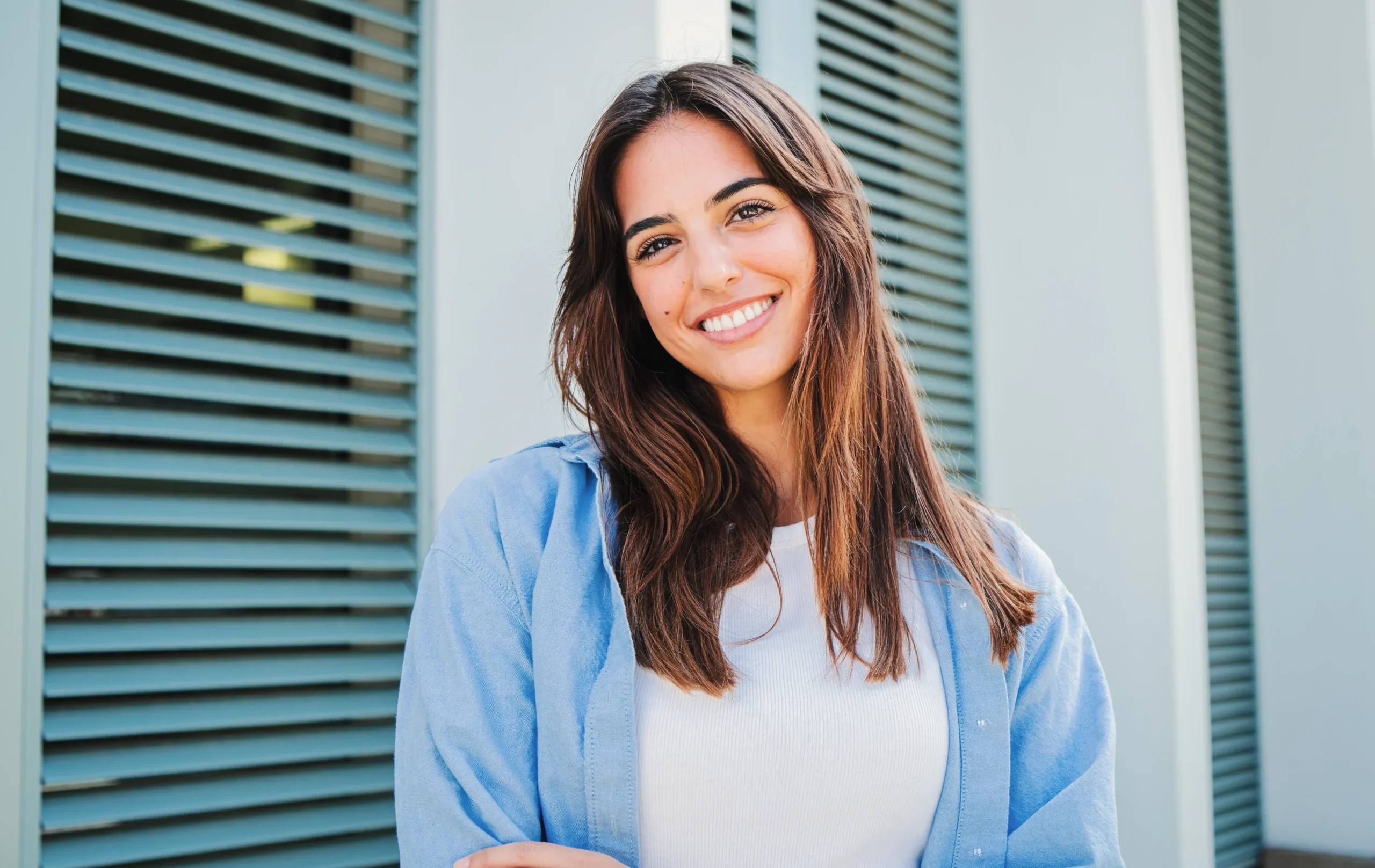 Smiling young woman standing outside in casual blue shirt.