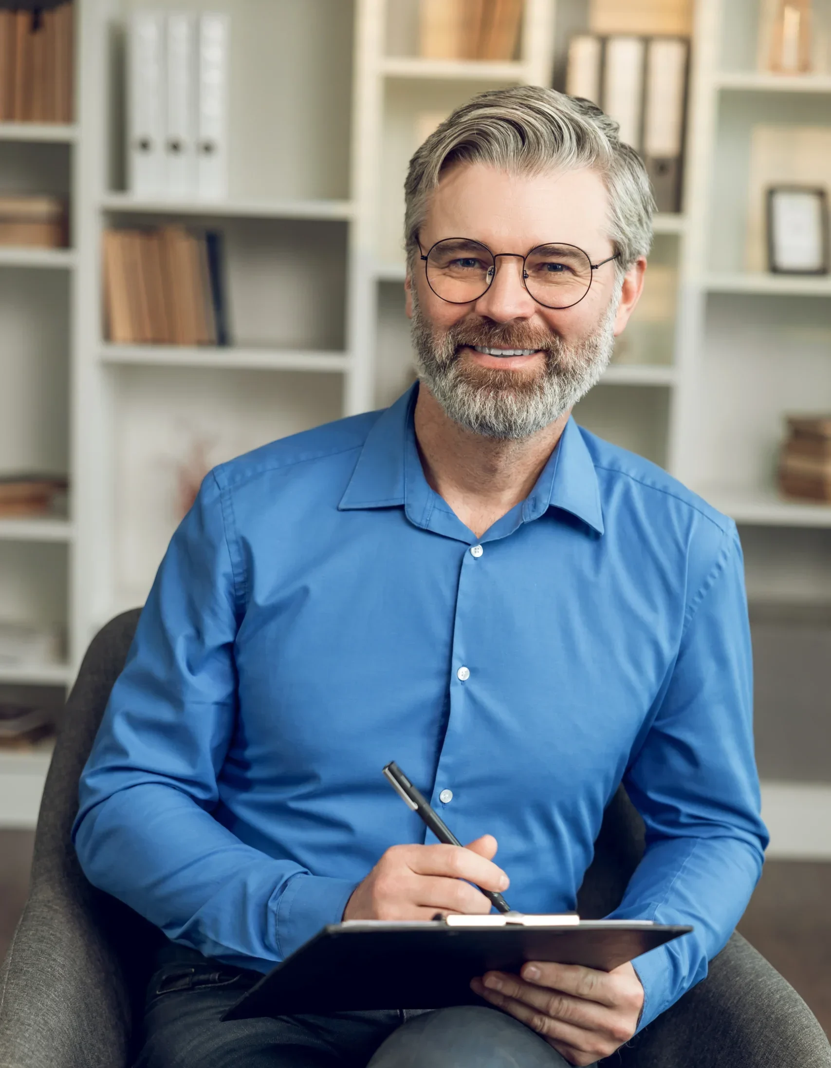 Smiling male psychotherapist holding a clipboard during an anxiety treatment session.