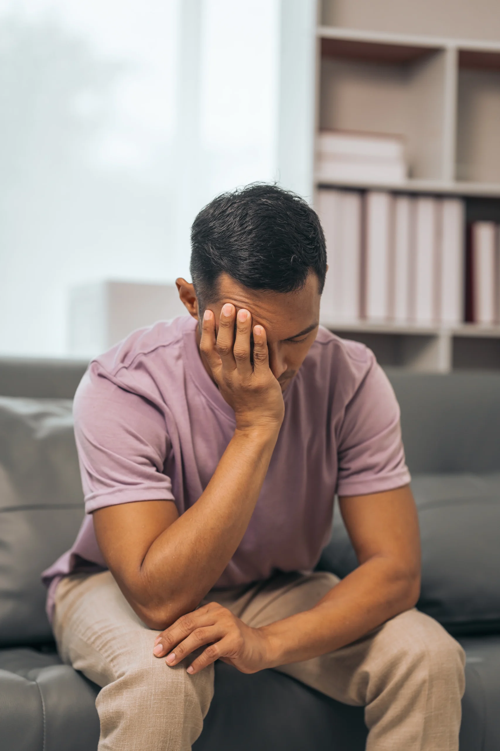 Man sitting on a couch with his head in his hand during a mental health treatment session.