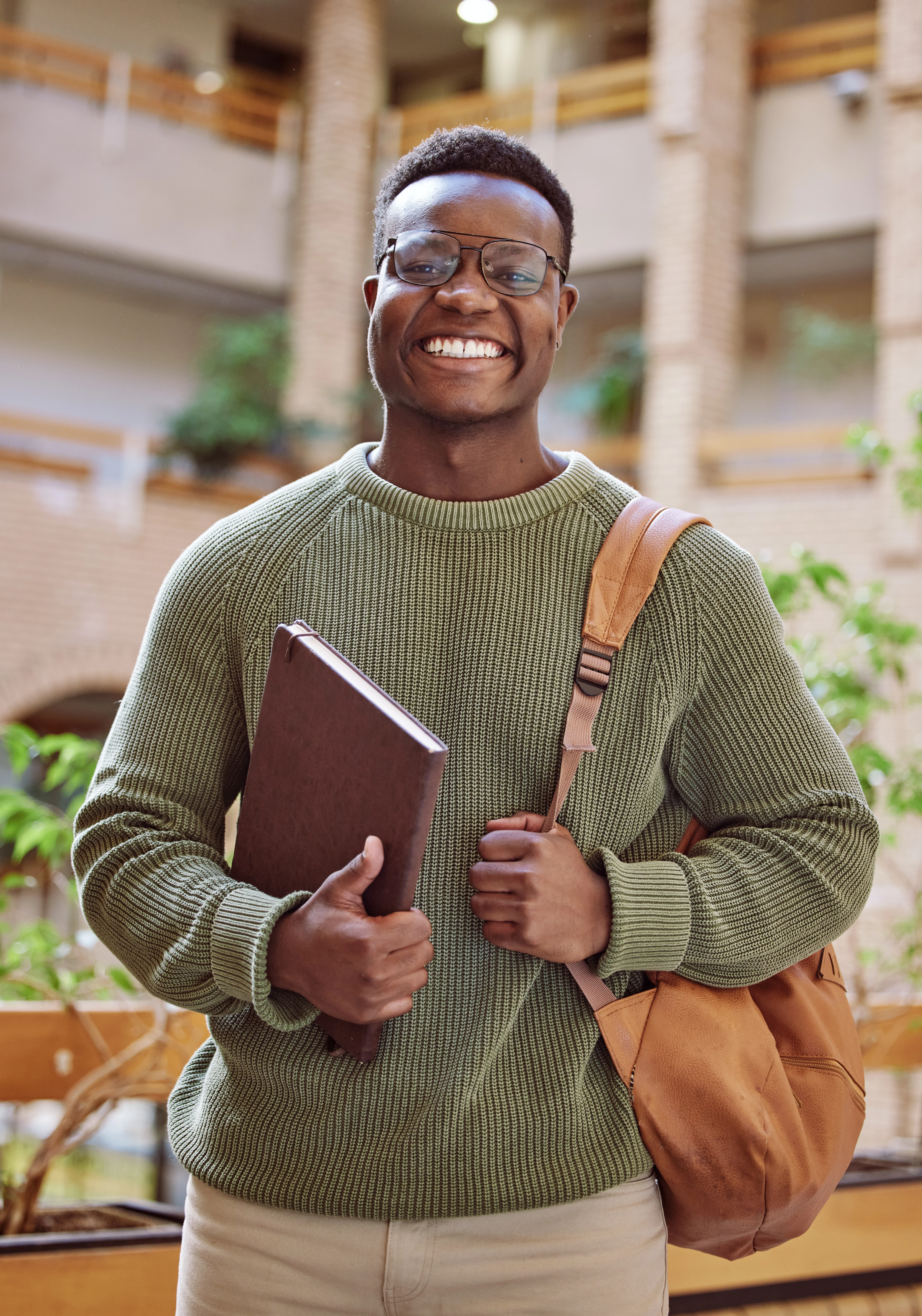 Smiling college student holding a notebook and backpack in a campus building.