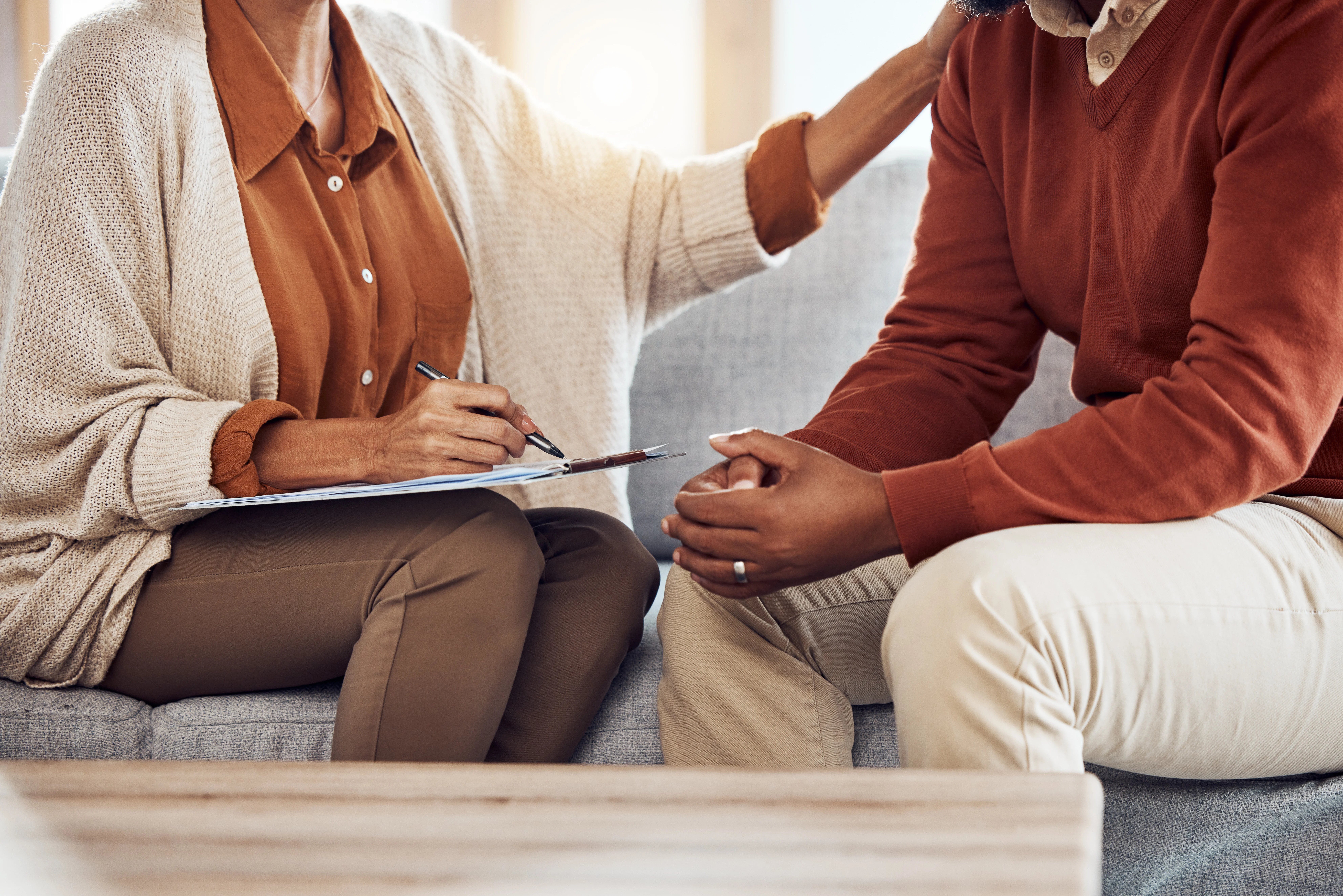 Supportive therapist taking notes while counseling an adult client during a mental health session.