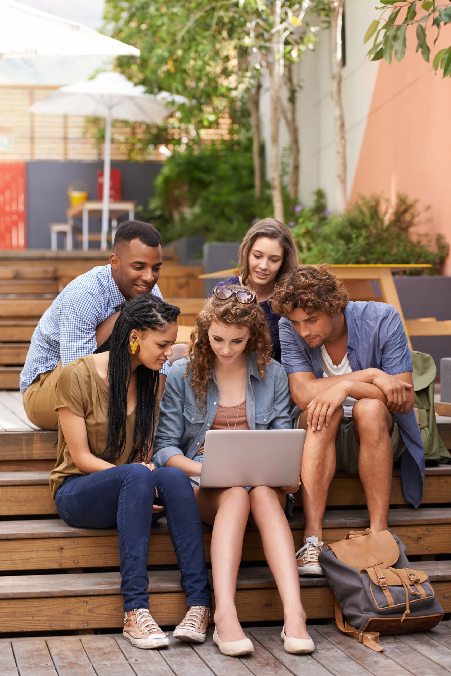 Diverse group of young adults sitting together outside and looking at a laptop.