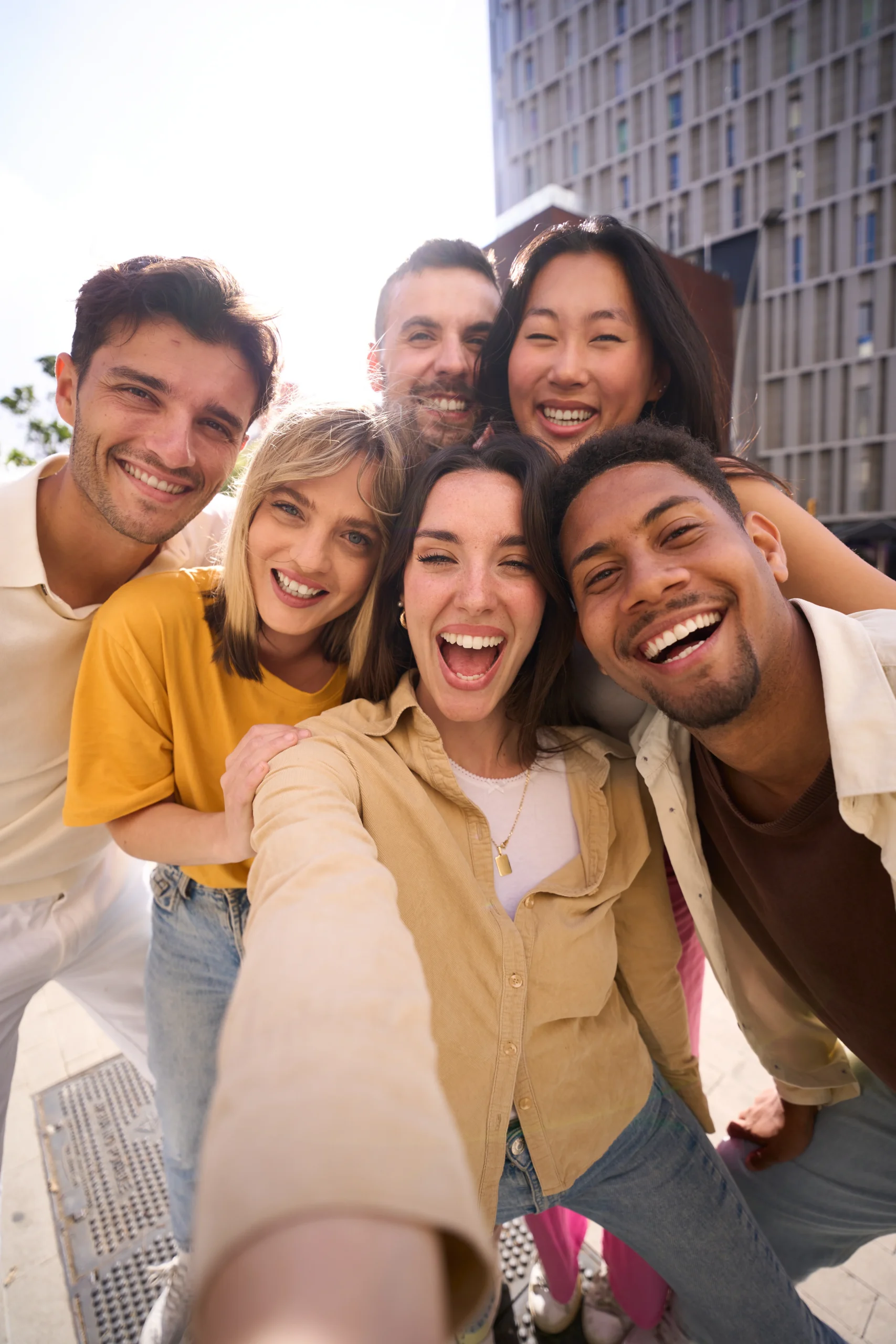 Group of diverse young adults smiling and taking a selfie outdoors together.