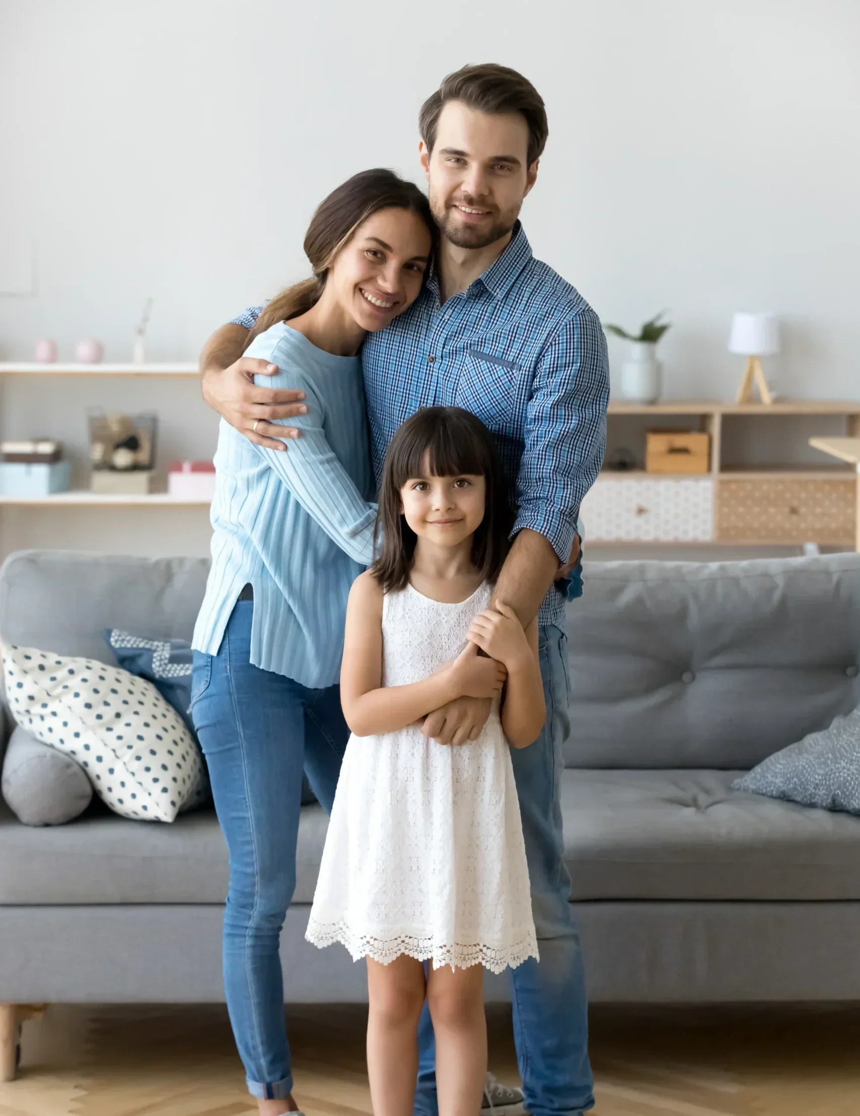 Smiling mother, father, and young daughter standing together in their living room.
