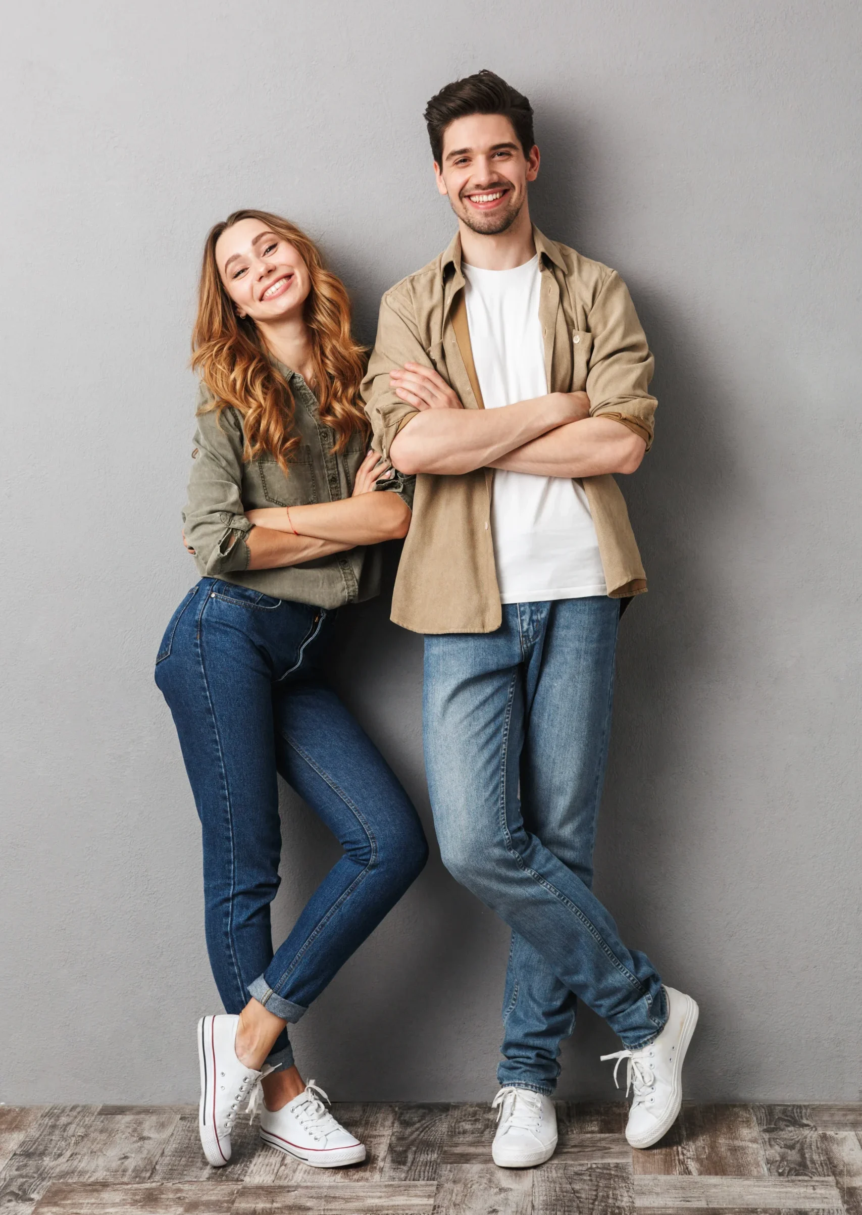 Smiling man and woman standing together against a gray wall.