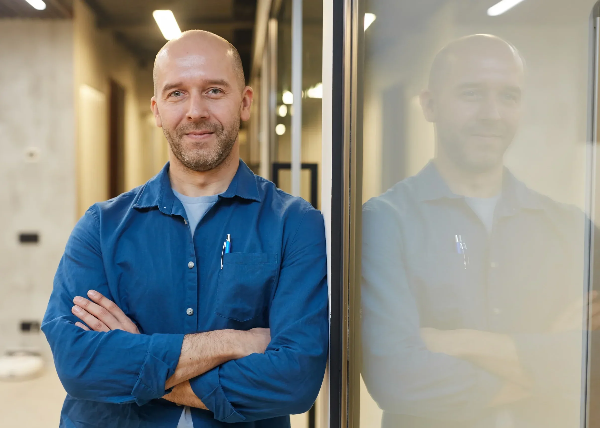 Smiling man standing confidently in an office hallway with arms crossed.
