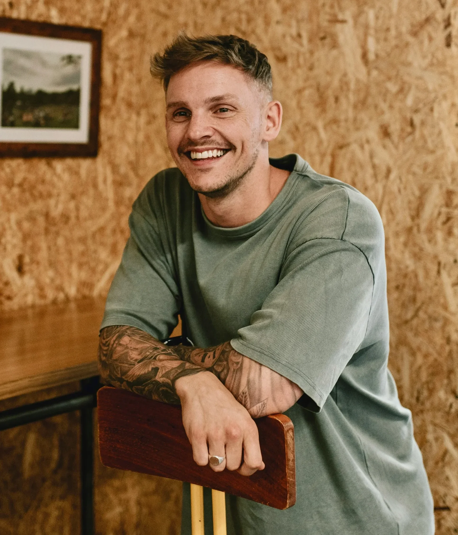 Smiling young man leaning on a chair in a relaxed, casual setting.