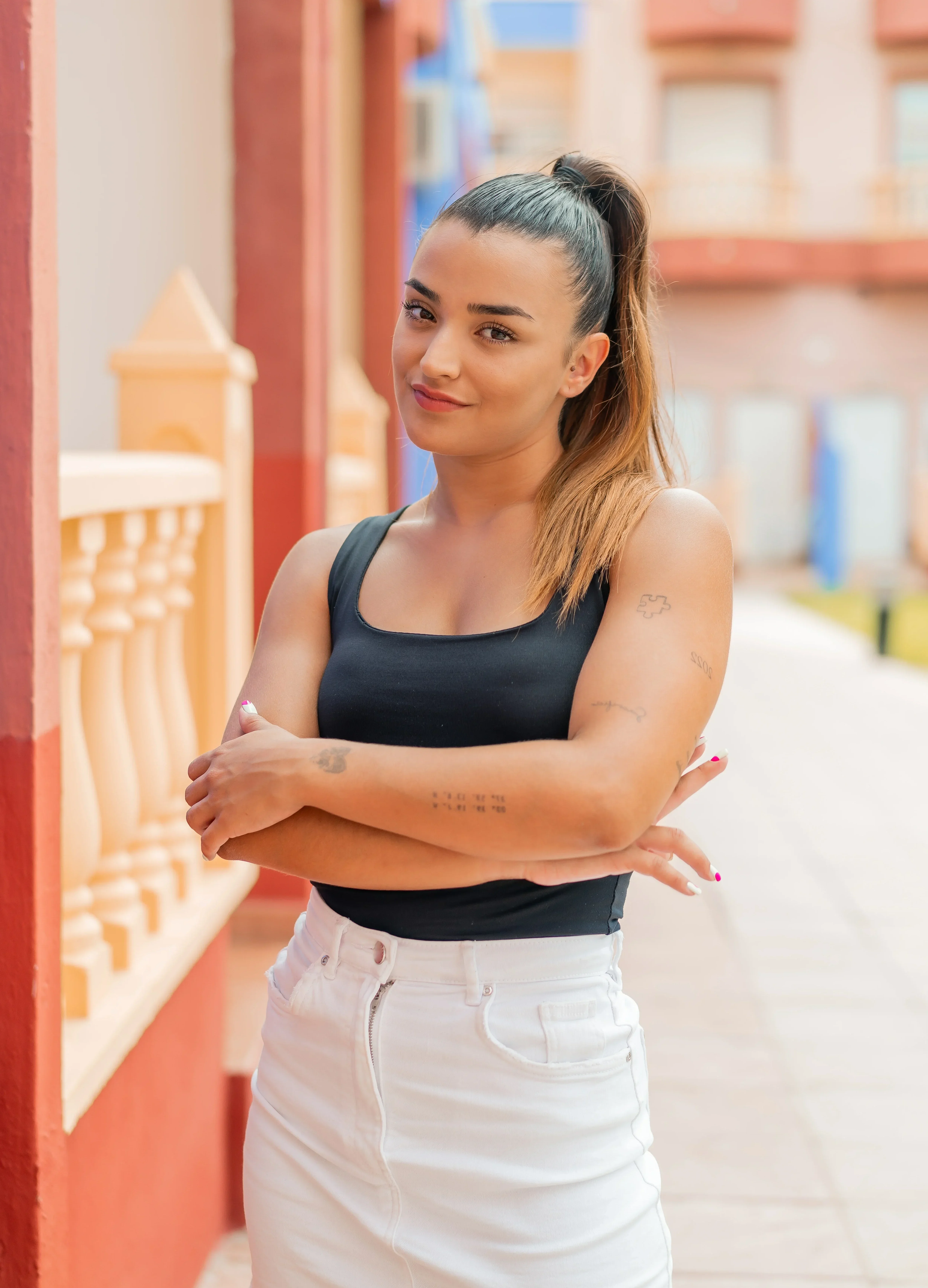 Young woman standing outdoors with arms crossed, smiling confidently in a residential courtyard.