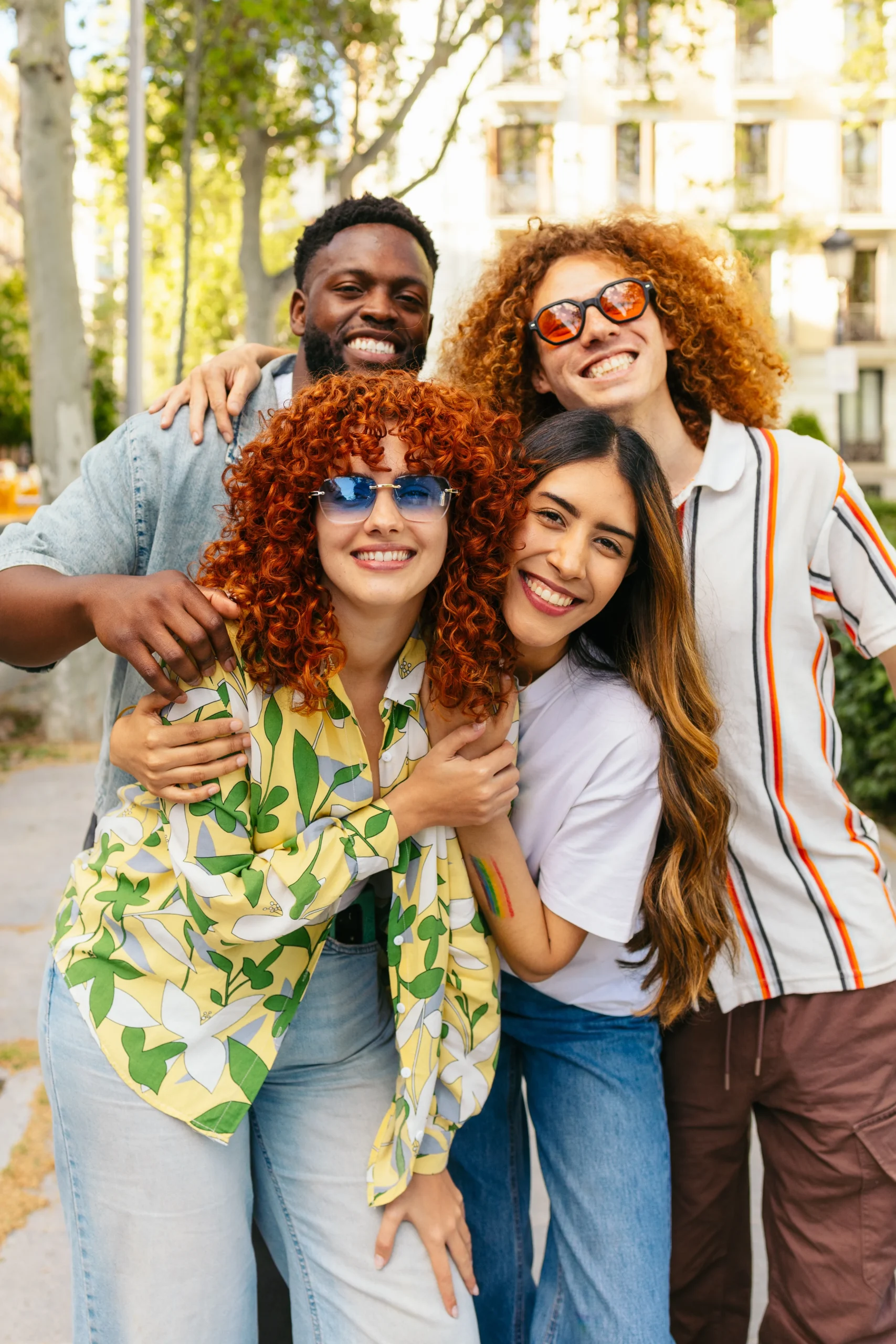 Group of diverse young adults smiling and embracing outdoors in a city park.