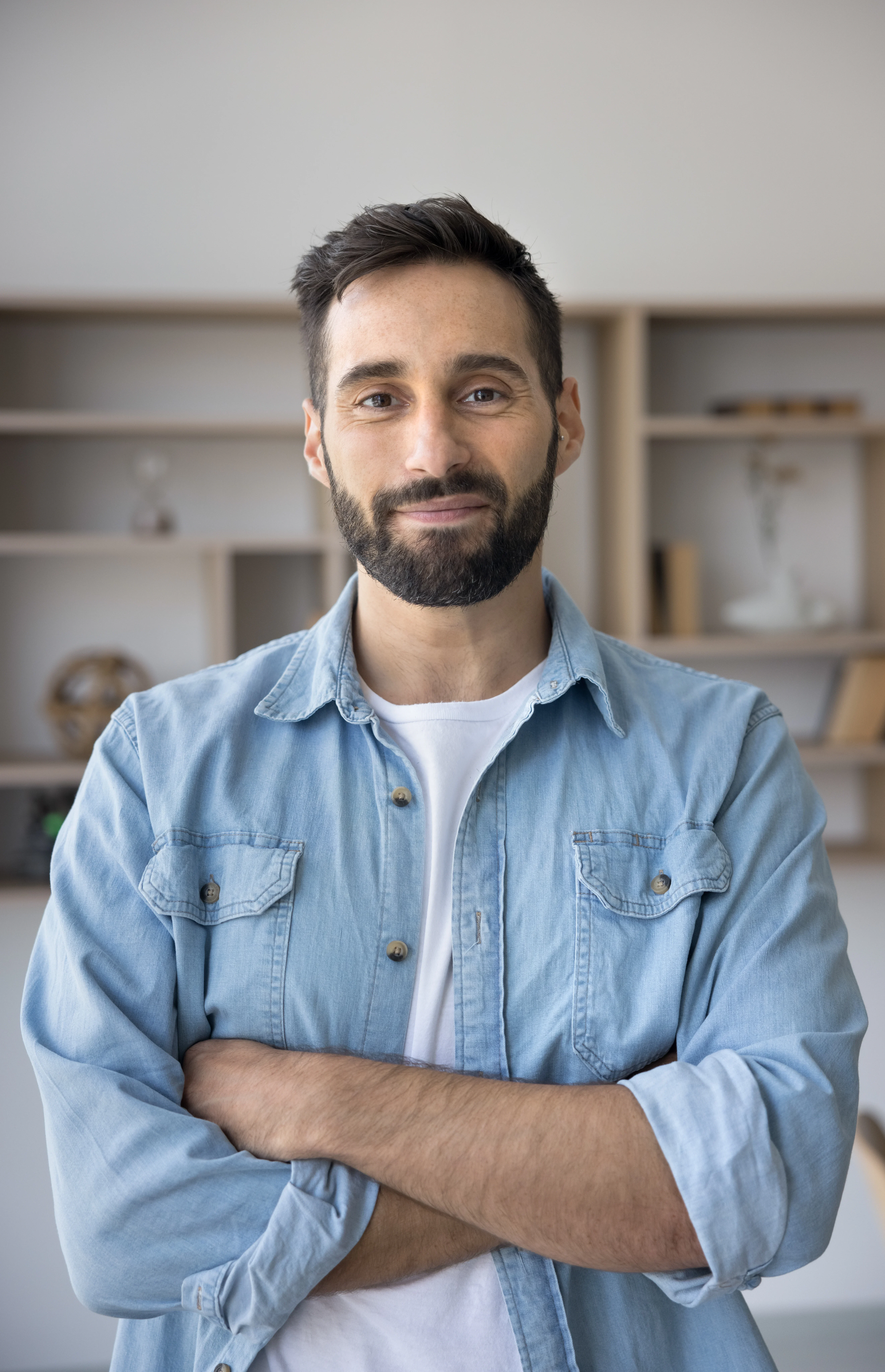 Confident young man standing indoors with arms crossed and smiling.