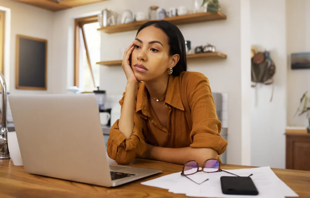 Woman sitting at a kitchen counter looking stressed while working on a laptop, representing adult ADHD and mental overload.