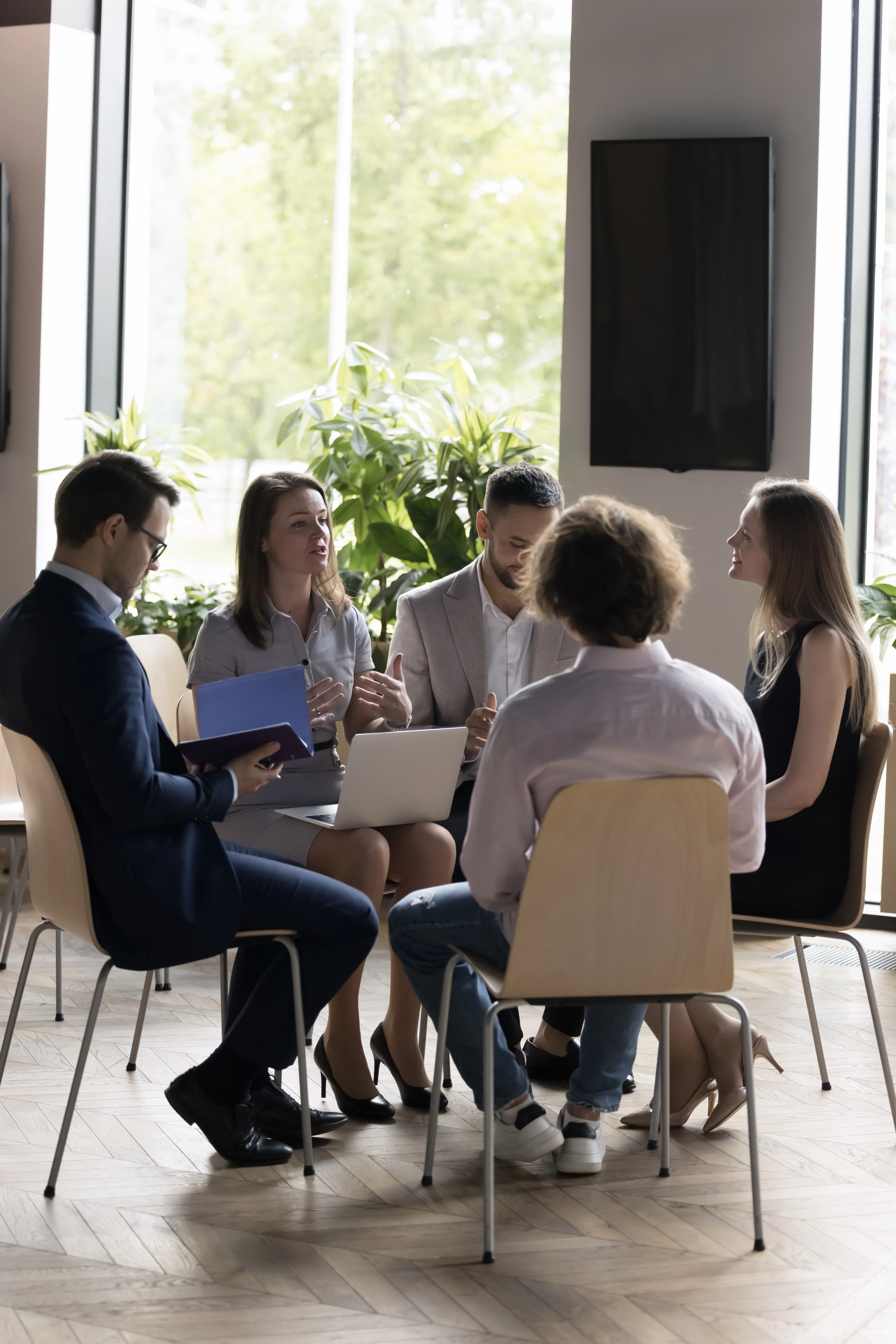 Adults sitting in a group therapy session having a discussion in a bright room.
