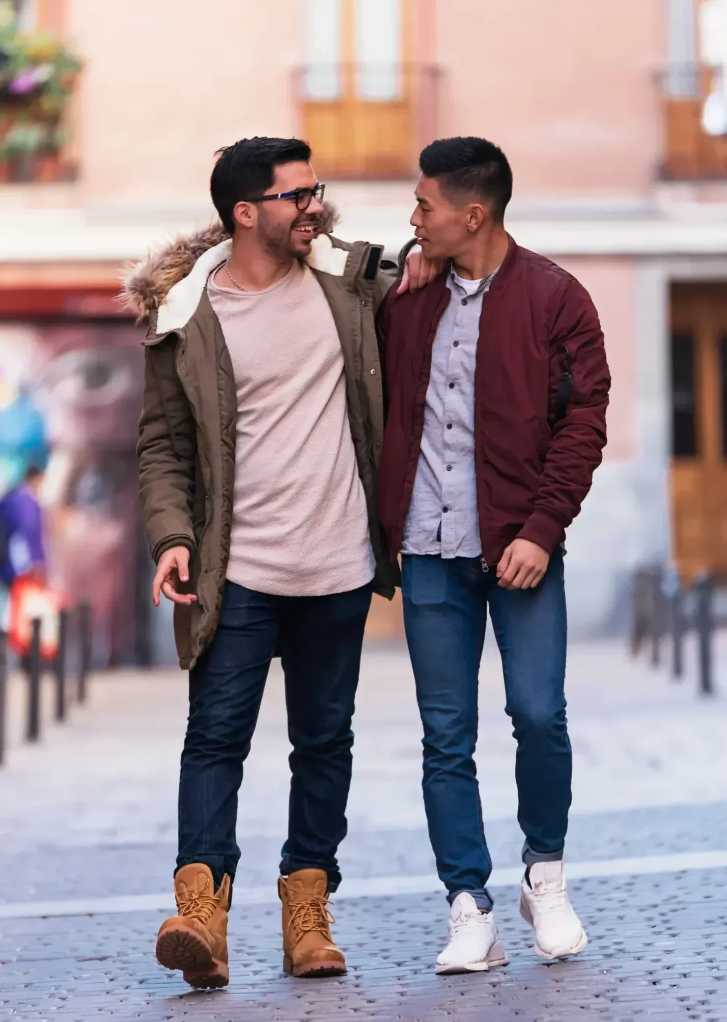 Two male friends walking together outdoors with arms around each other in a city street setting.