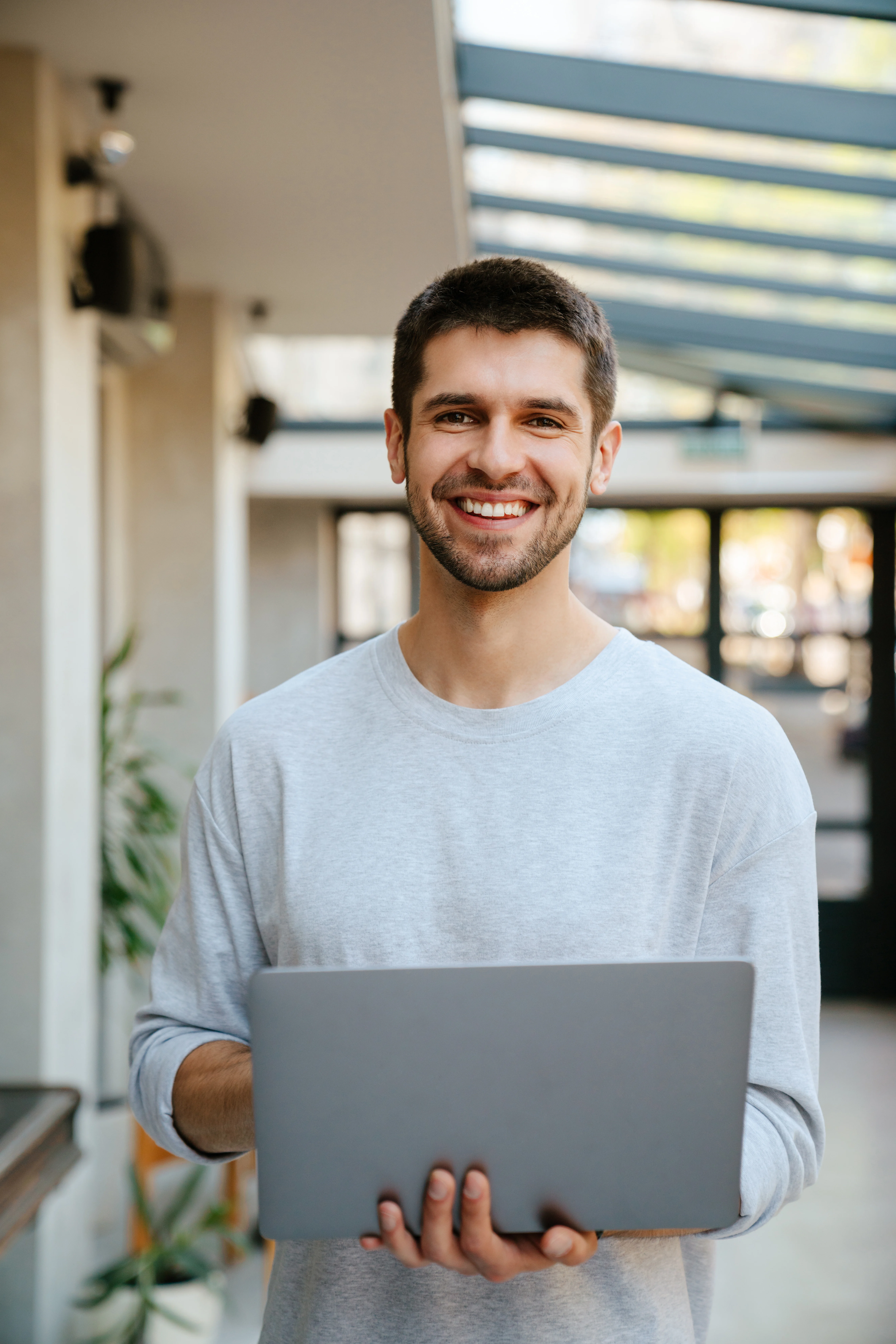 Smiling man holding a laptop in a bright modern indoor space