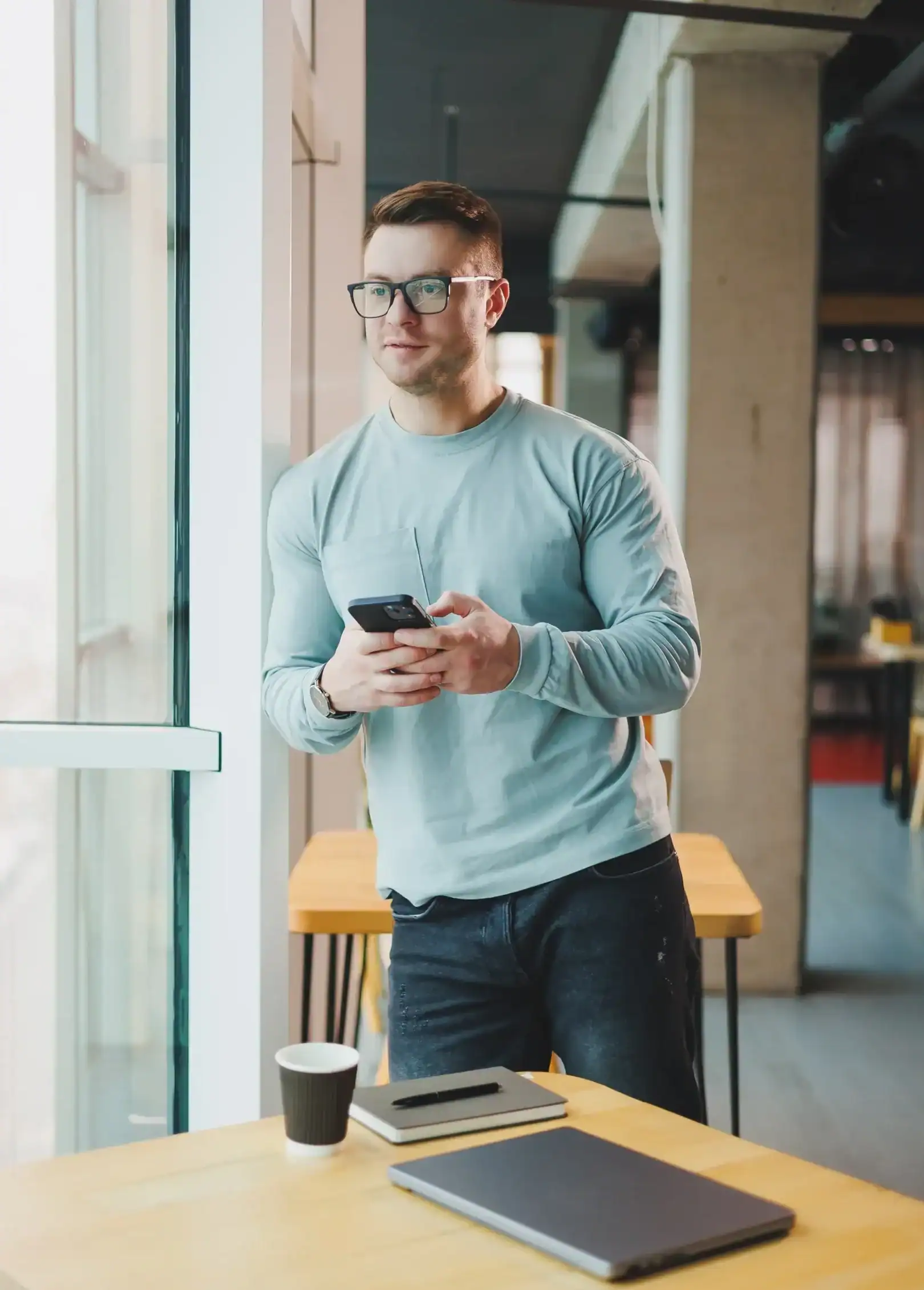 Adult man standing by a window using a smartphone in a modern indoor setting