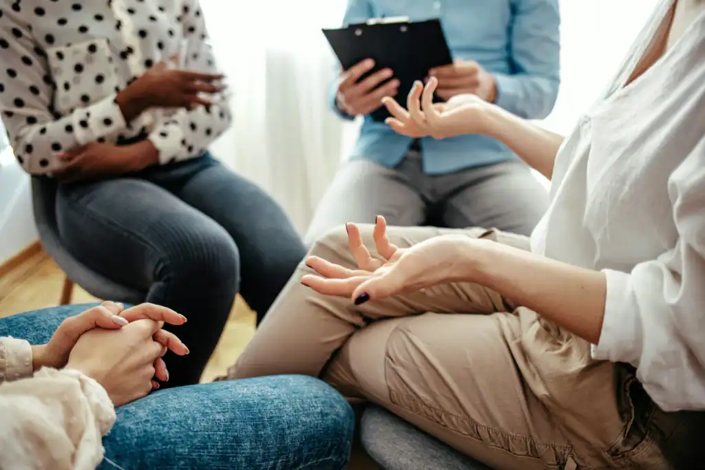Participants talking during a group therapy session while a therapist takes notes