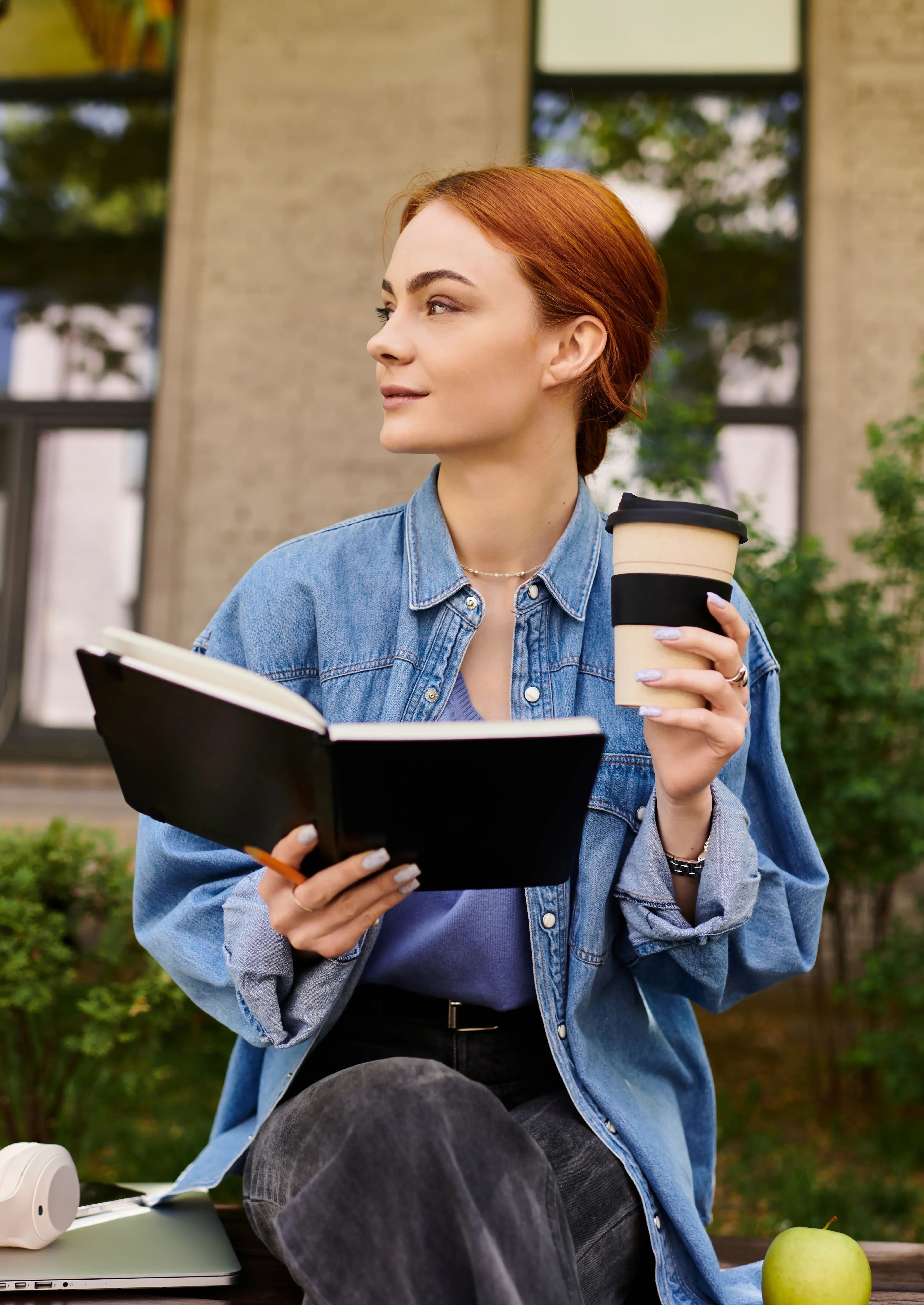 Woman holding a journal and coffee while sitting outdoors