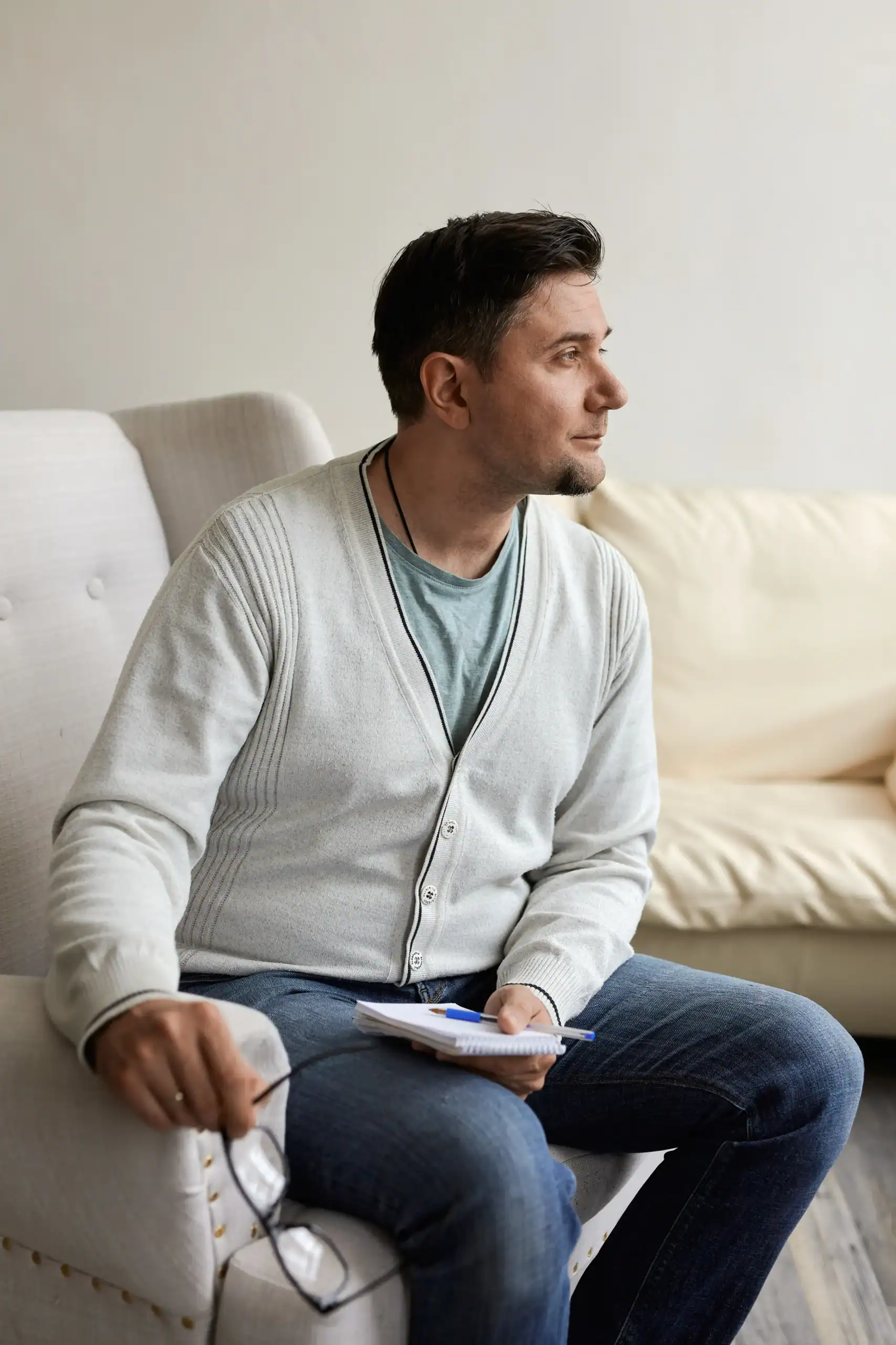Man sitting in a chair holding a notebook and looking off to the side