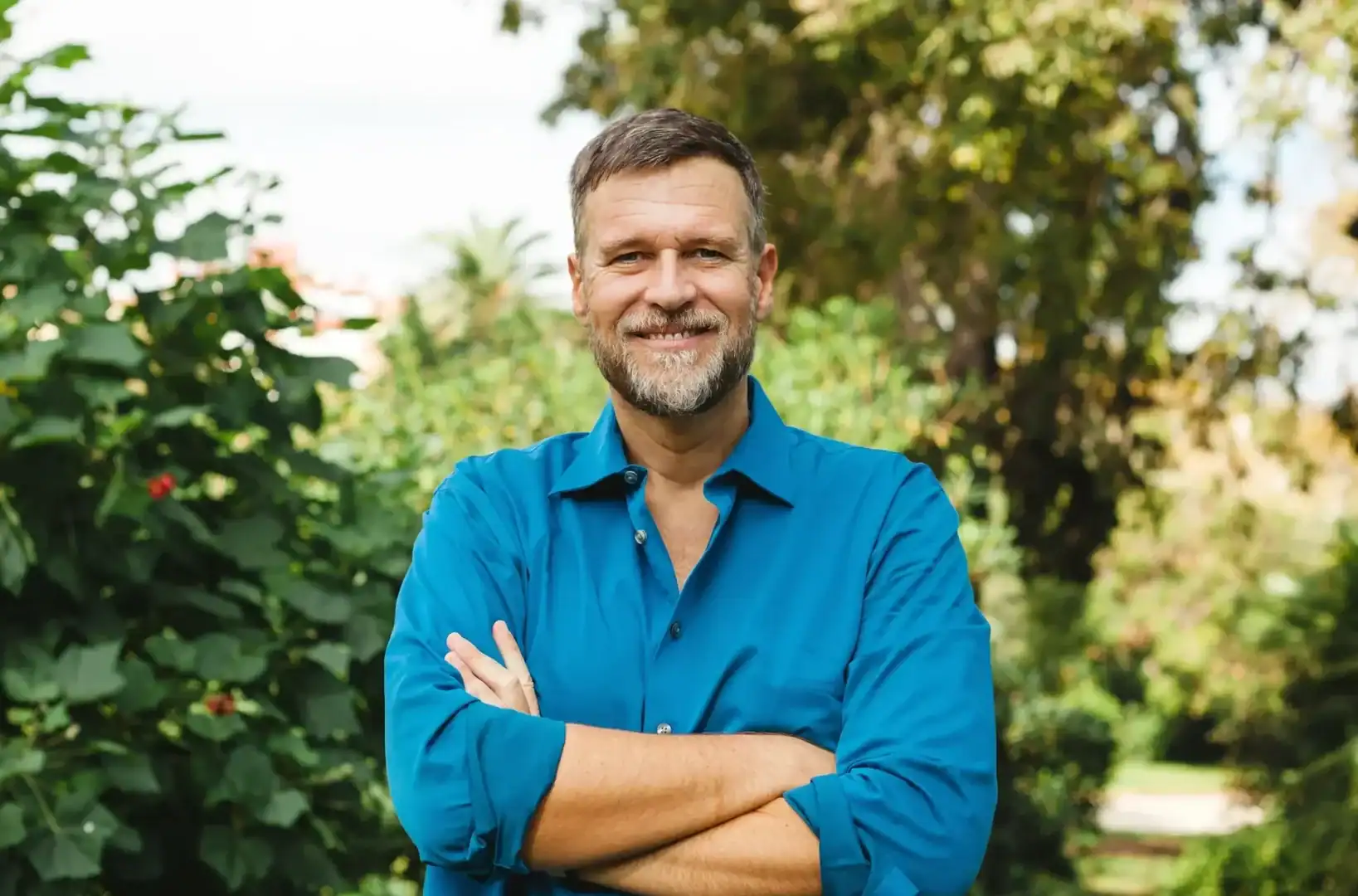 Man smiling outdoors with arms crossed