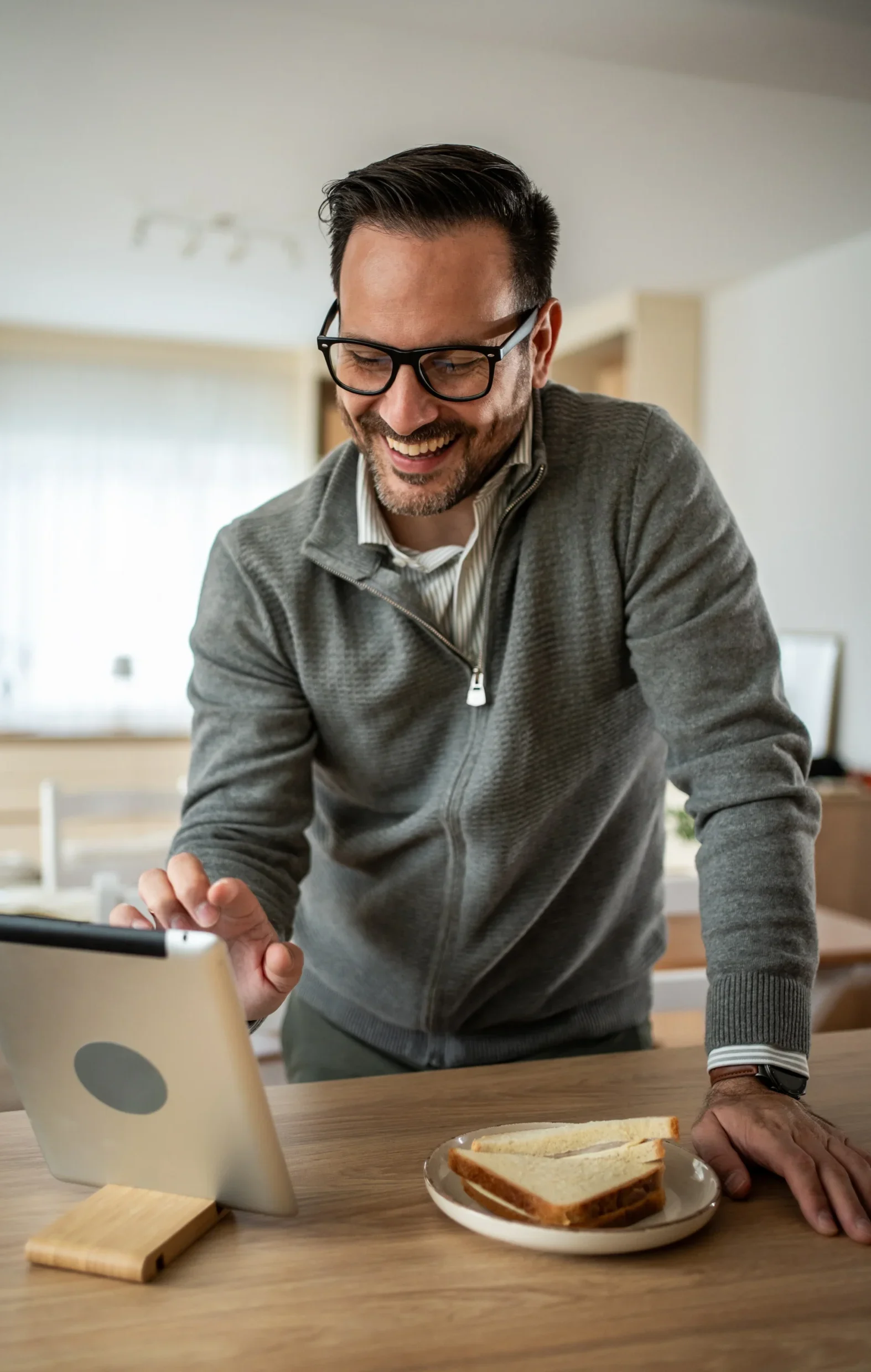 Smiling man using a tablet at a kitchen counter with breakfast on the table