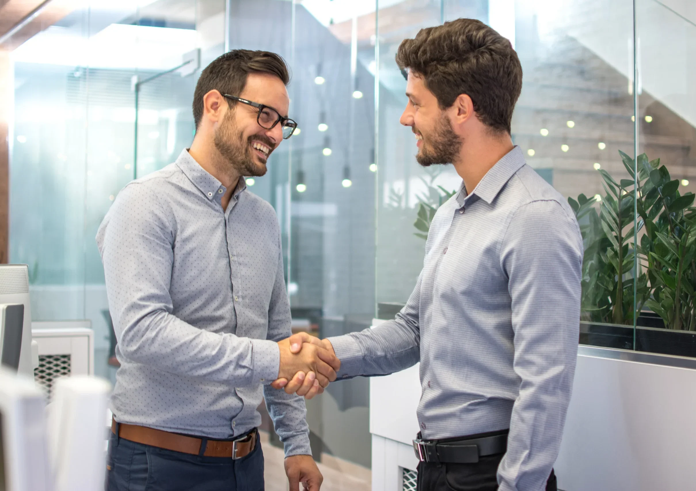 Two men shaking hands in a modern office setting, representing partnership and professional trust