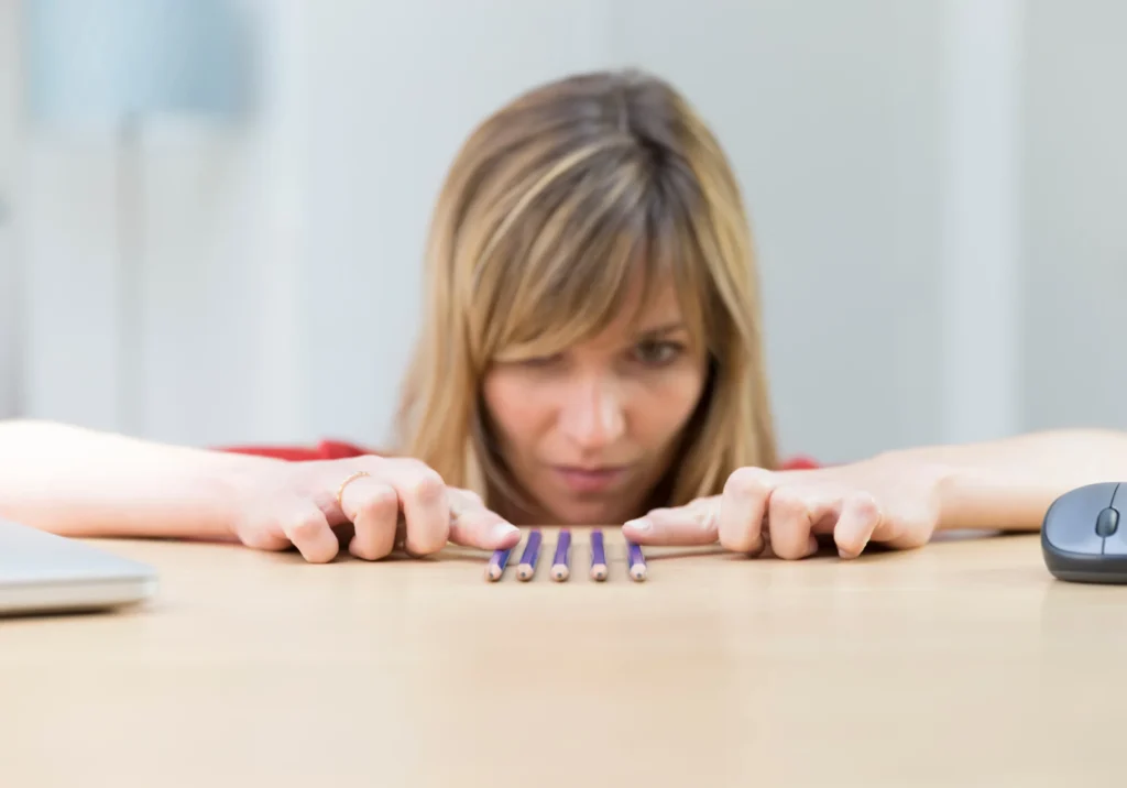 Woman carefully aligning pencils on a desk, demonstrating obsessive-compulsive behavior and need for symmetry.
