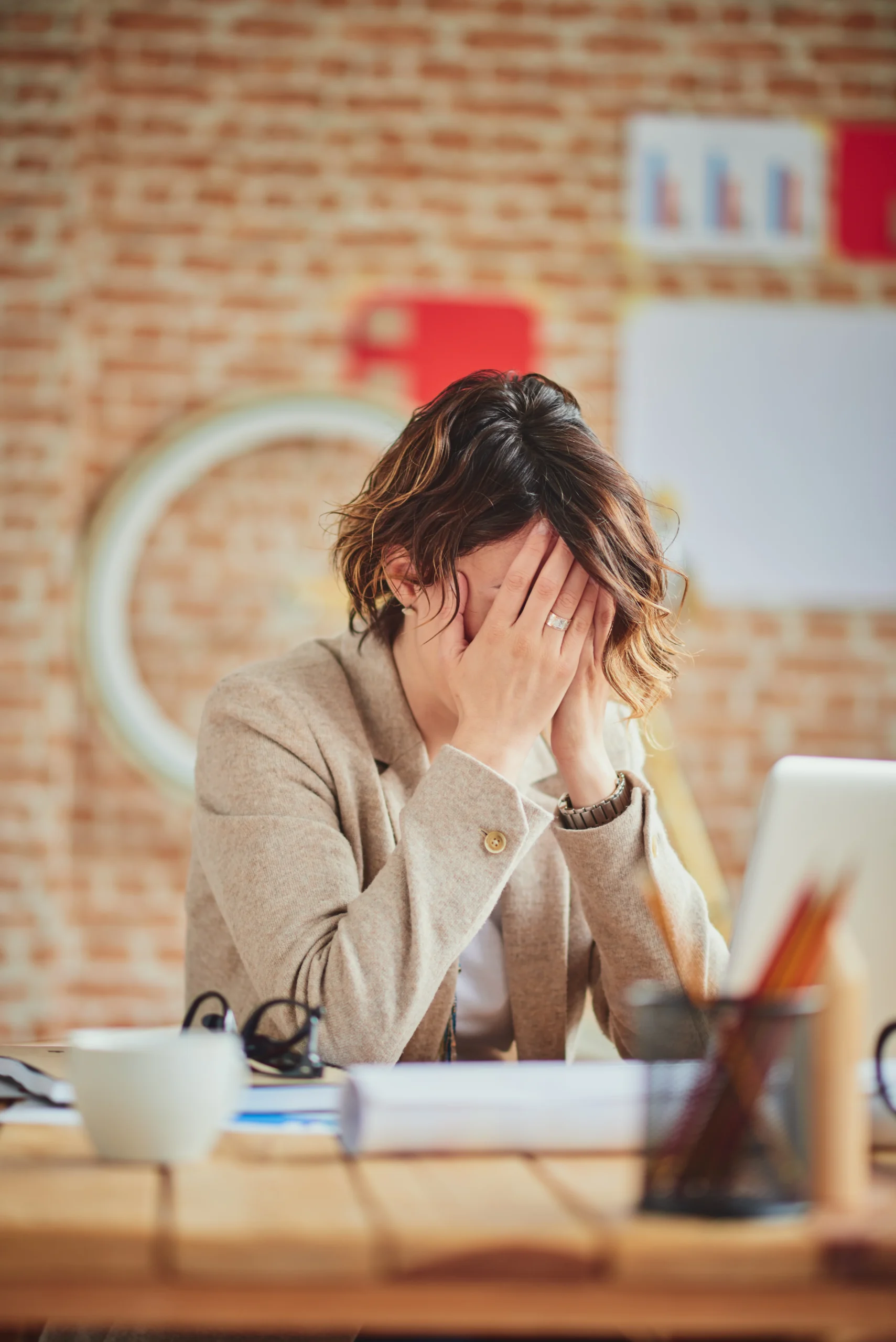 Adult sitting at a desk with hands covering face, appearing overwhelmed by intrusive thoughts related to obsessive-compulsive disorder (OCD).
