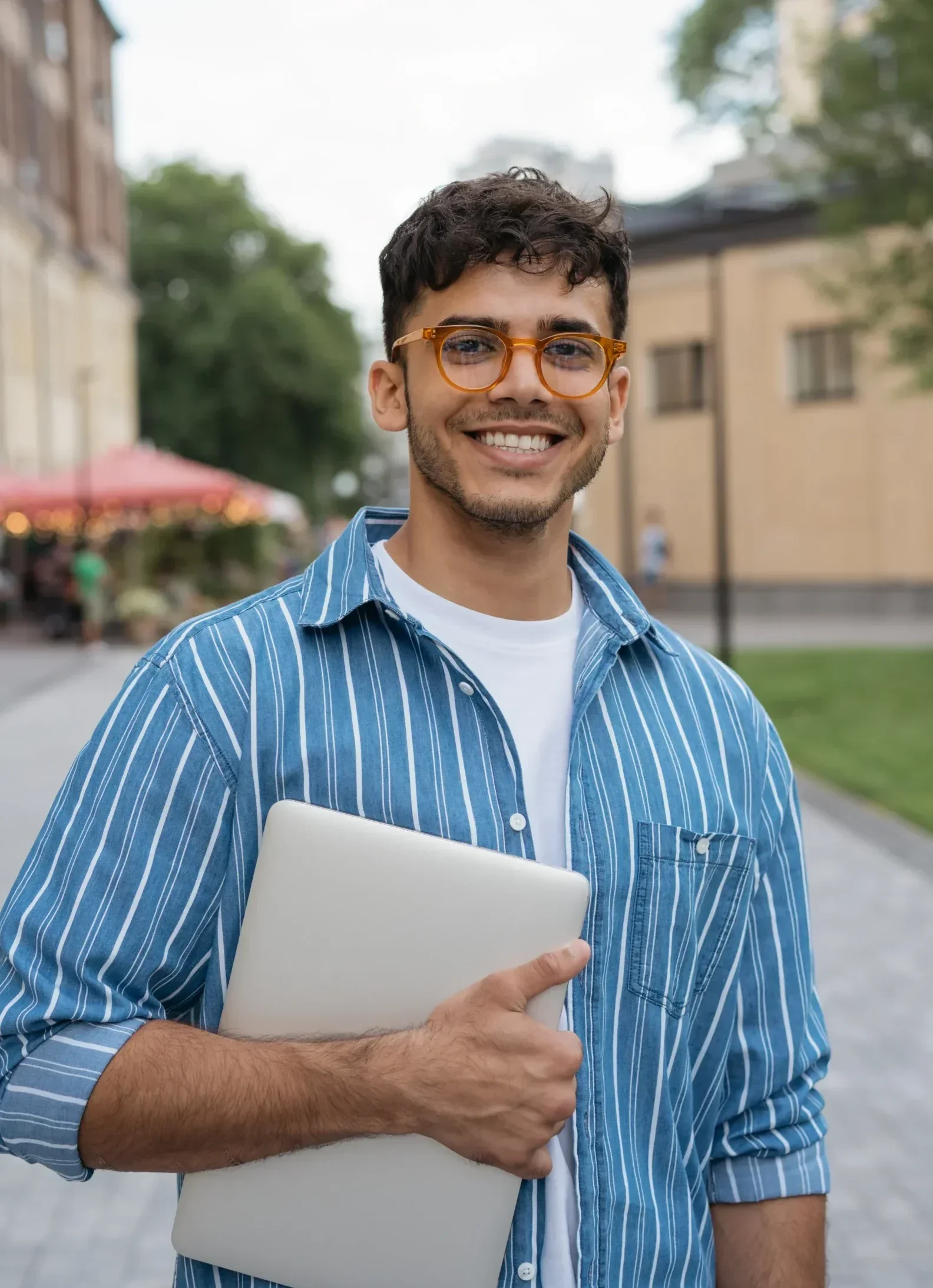 Young adult smiling outdoors holding a laptop