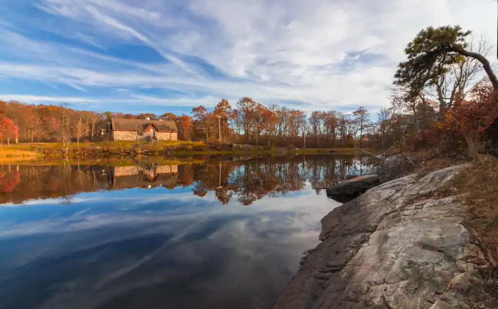 Veterans Memorial Lodge at High Point State Park reflected in a calm lake with autumn trees and a rocky shoreline