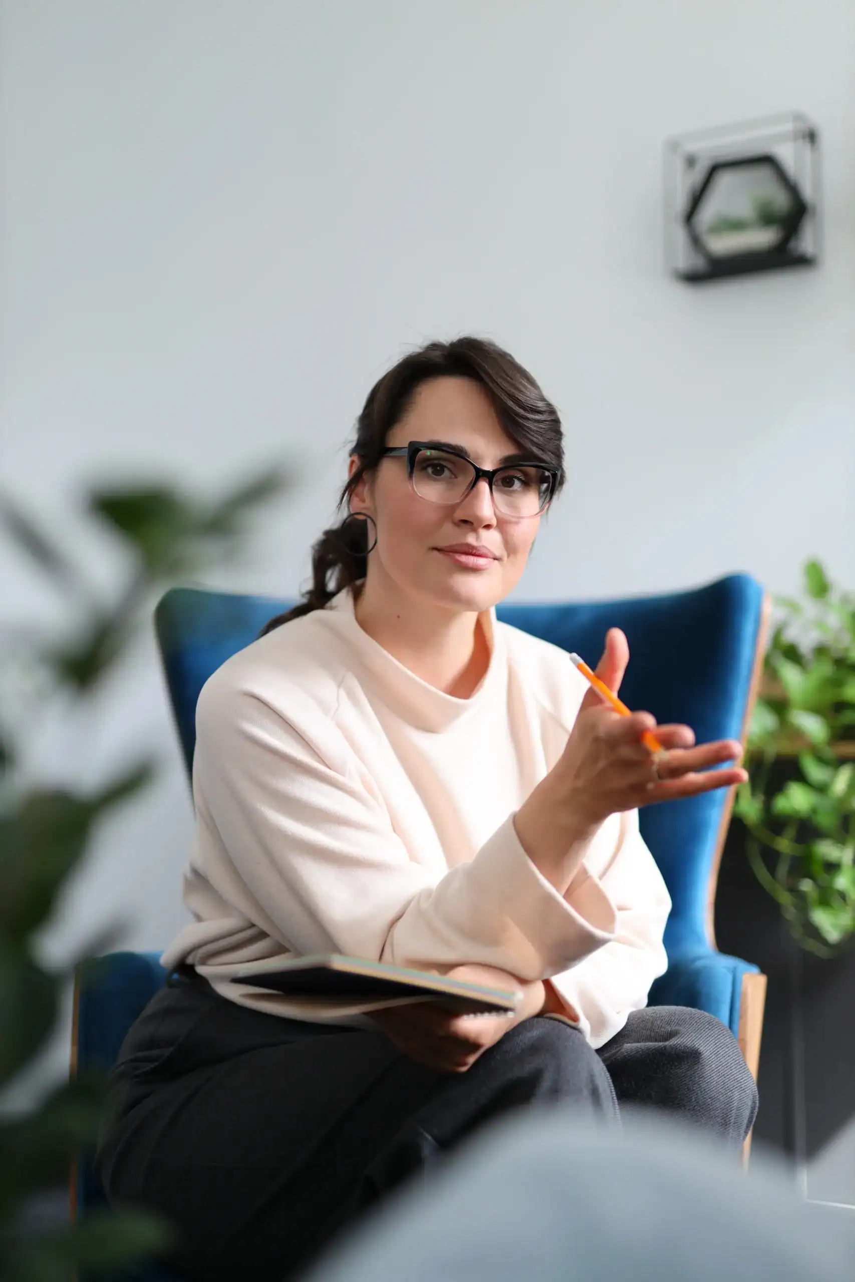 Mental health clinician holding a notebook and gesturing while speaking in a calm office setting