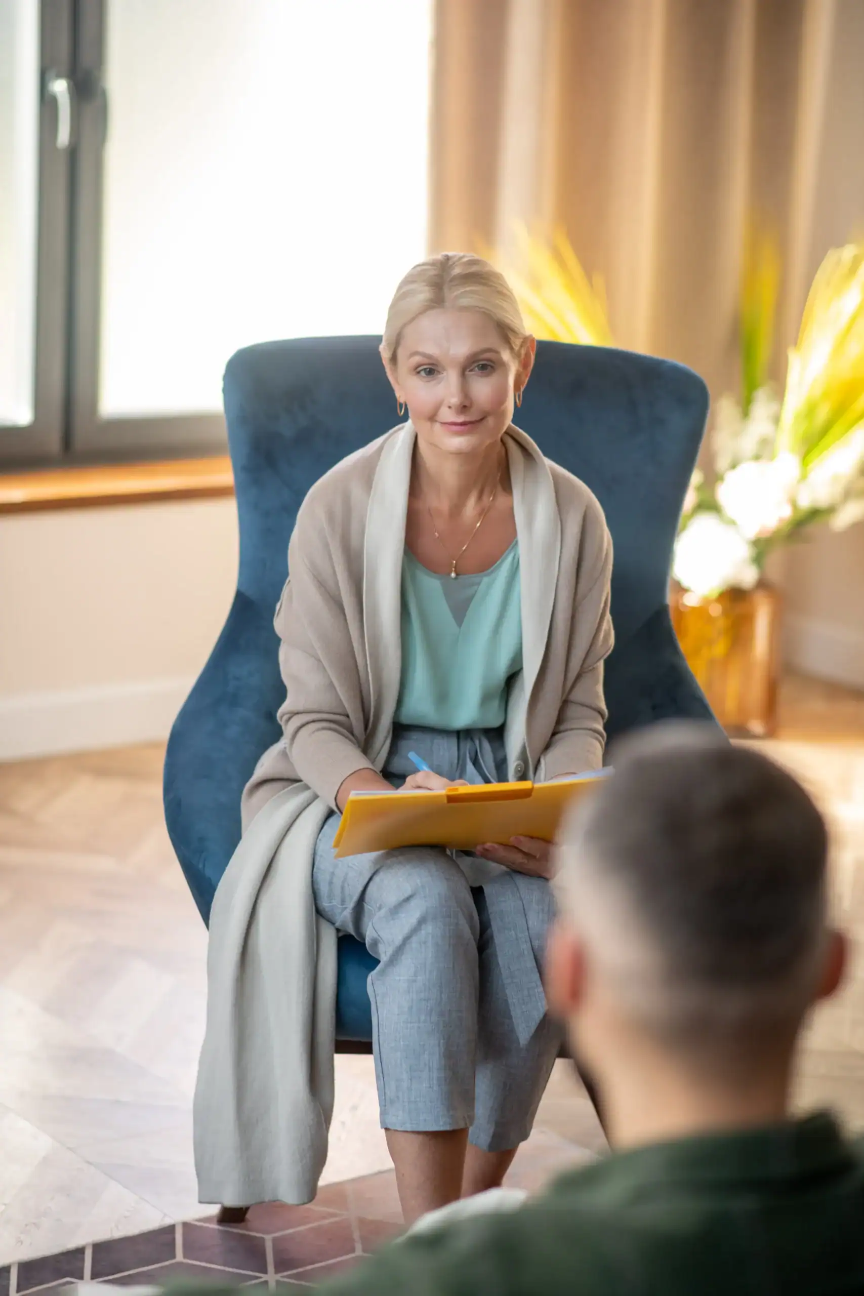 Therapist holding a clipboard during a counseling session with a client in a comfortable office.