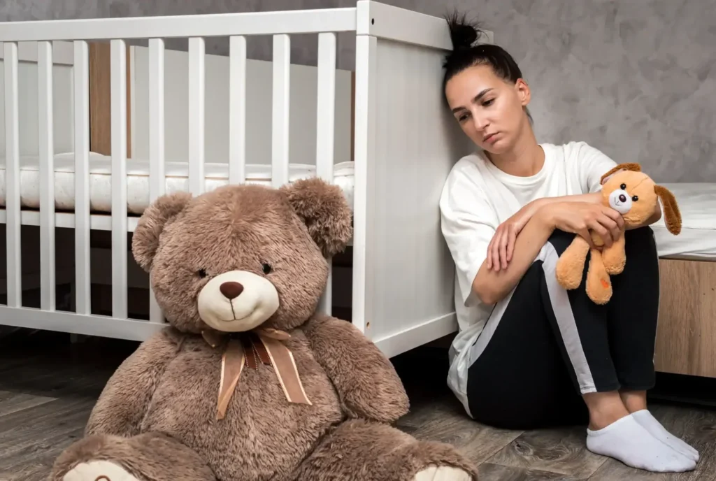 Mother sitting beside a crib in a nursery showing signs of postpartum depression