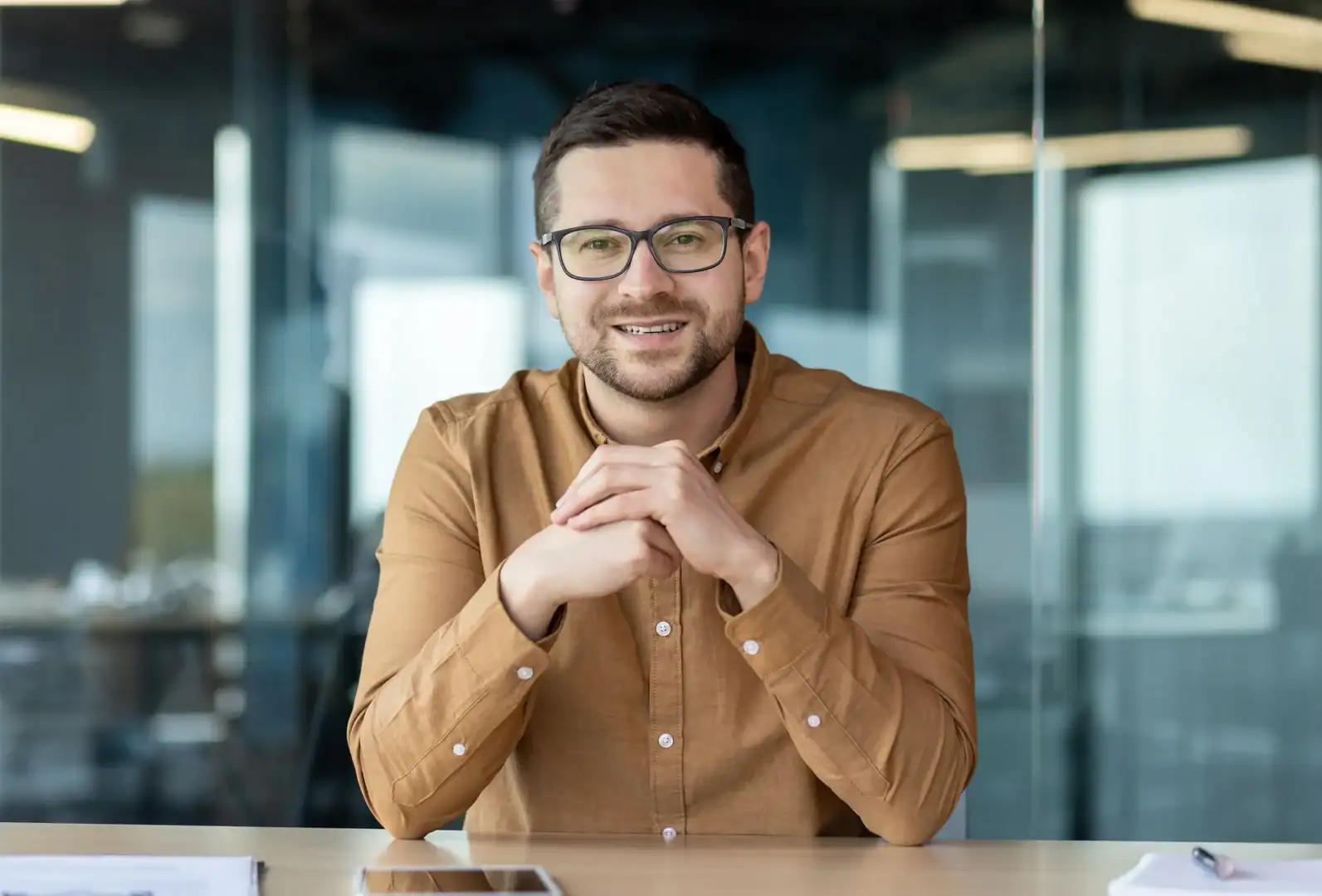 Smiling man wearing glasses seated at a conference table in a modern office