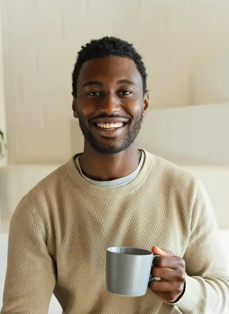 Smiling man holding a coffee cup while sitting indoors with a phone in hand