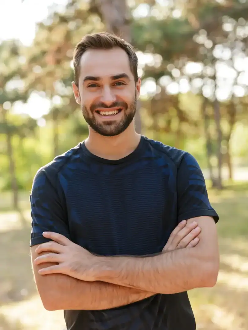 Smiling man standing outdoors with arms crossed