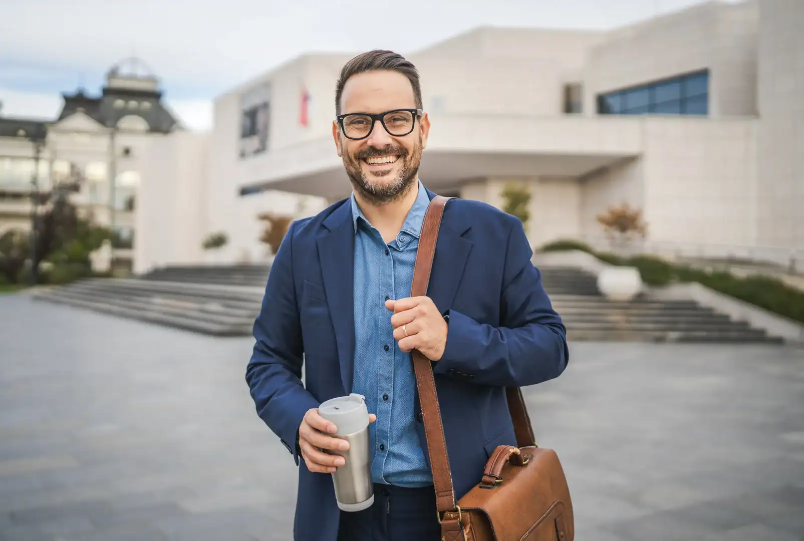 Smiling professional man outdoors holding a travel mug and shoulder bag