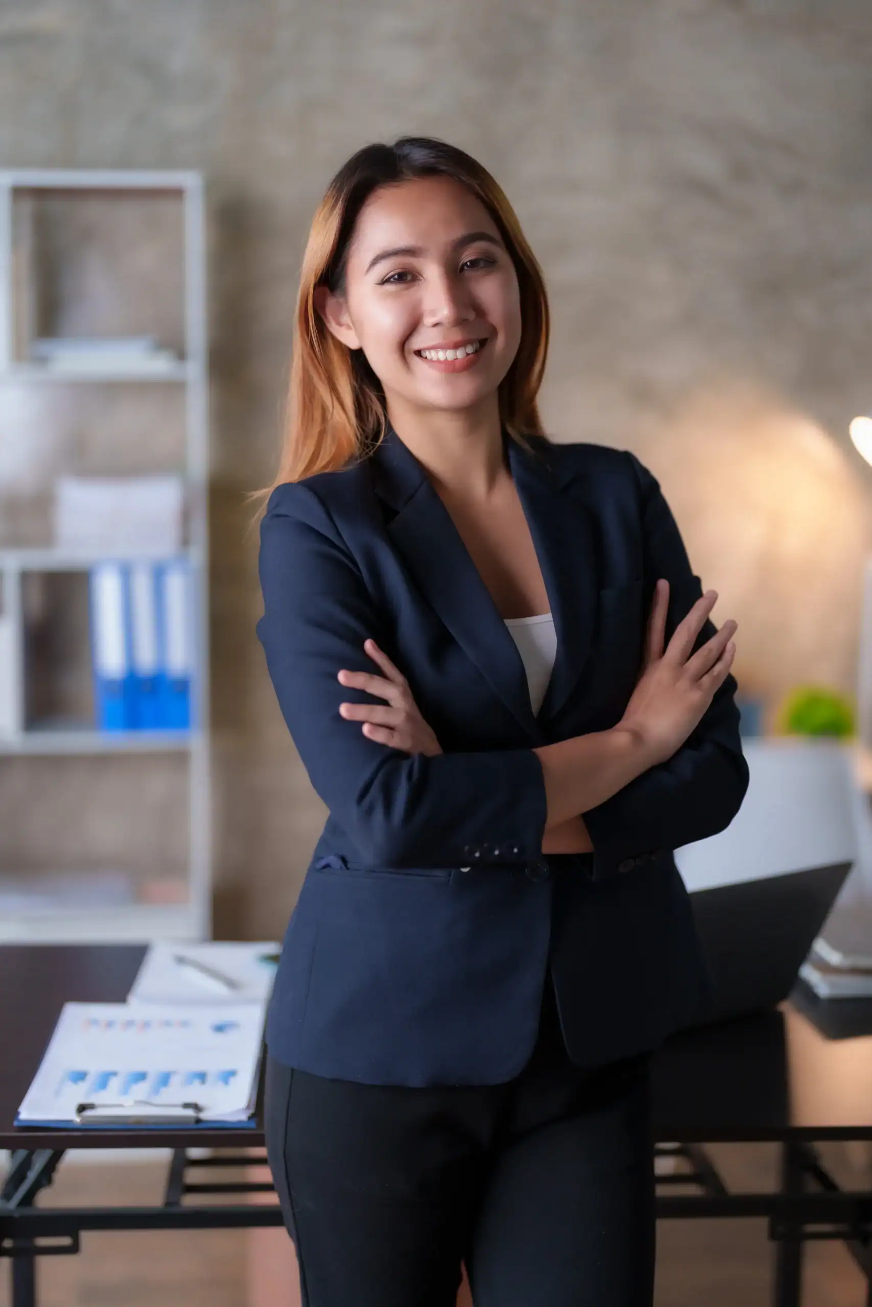 Woman in a blazer smiling in an office setting with desk in the background