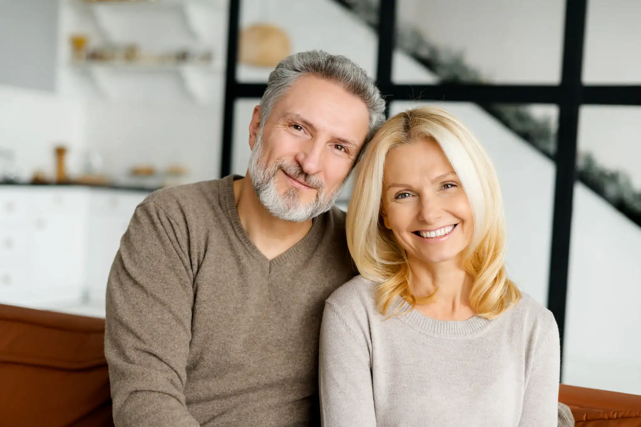 Smiling middle-aged couple sitting together at home, showing support and connection.