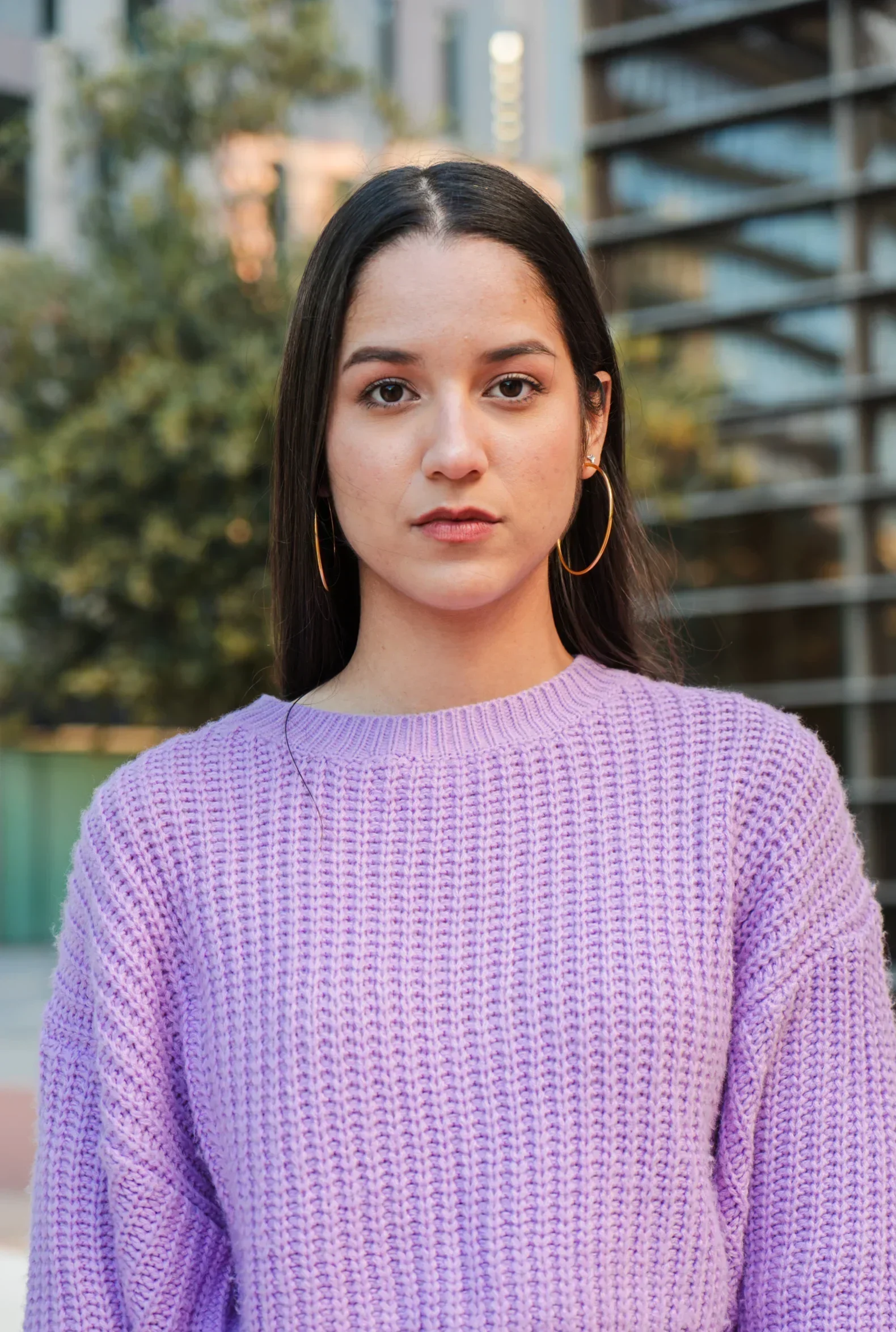 Young woman in a purple knit sweater standing outside near modern buildings