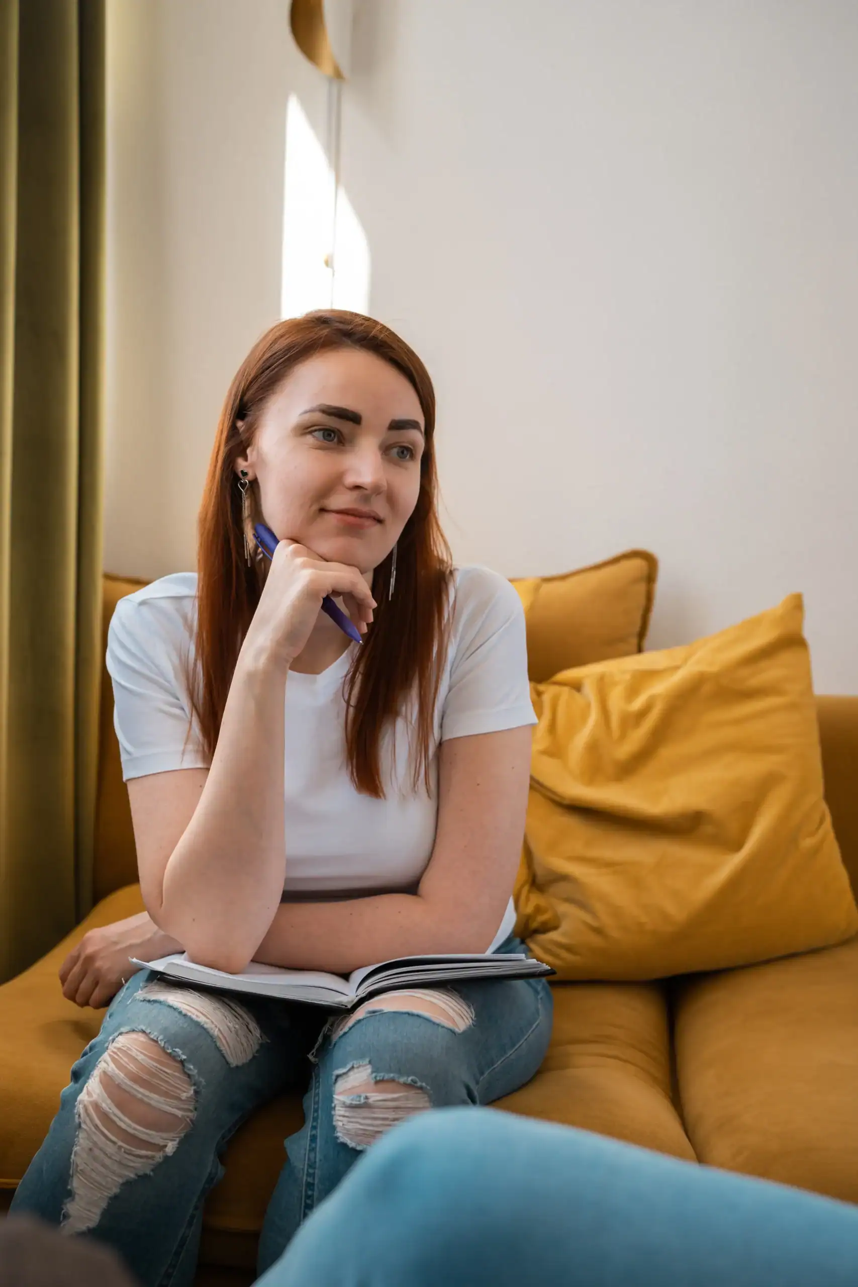 Woman sitting on a couch holding a pen and notebook during a therapy session