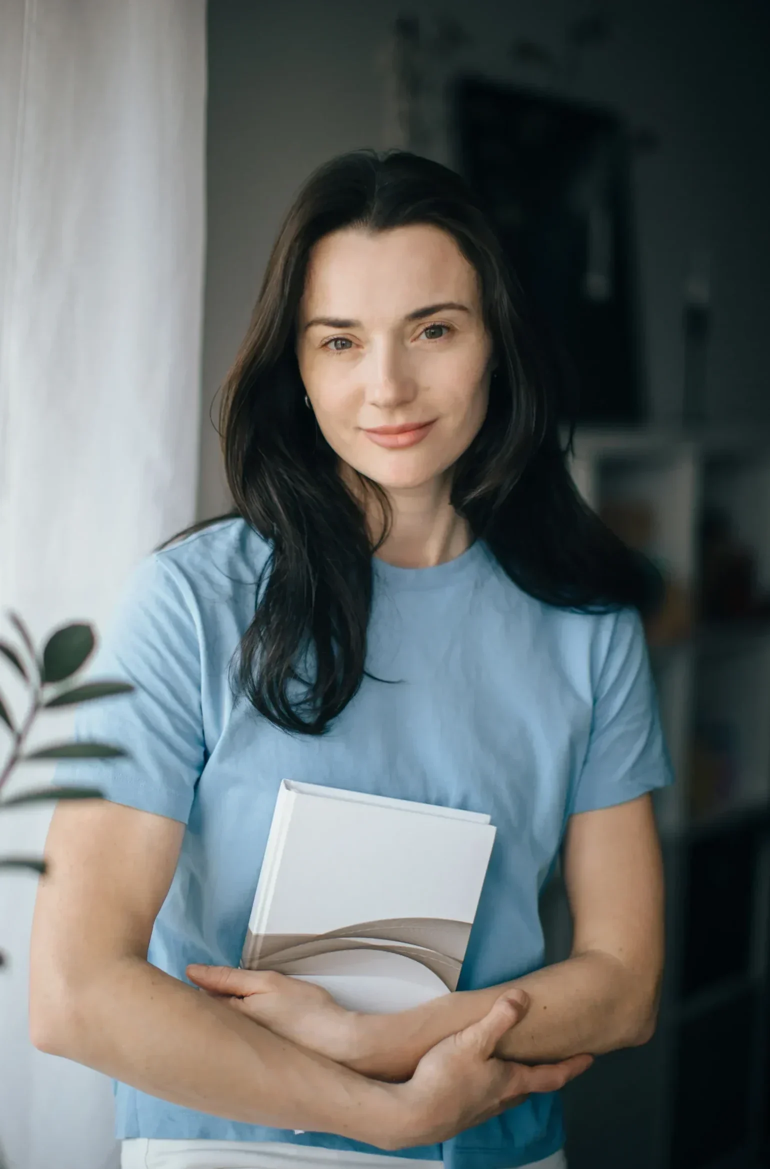 Woman holding a book and standing by a window in natural light