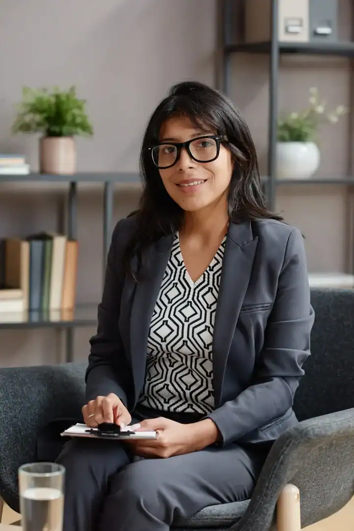 Professional woman wearing glasses holding a clipboard while seated in an office