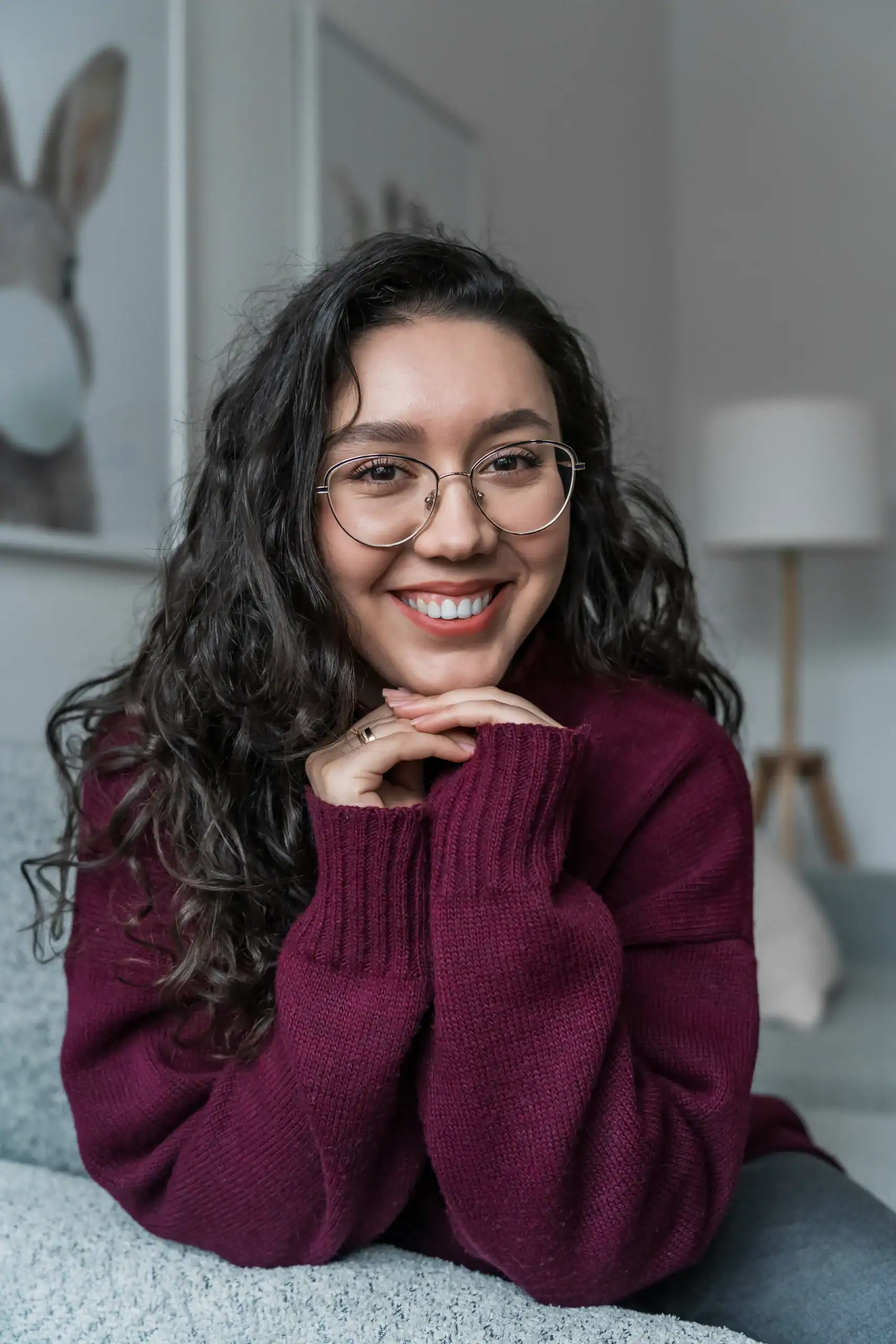 Woman smiling with hands under chin while wearing glasses