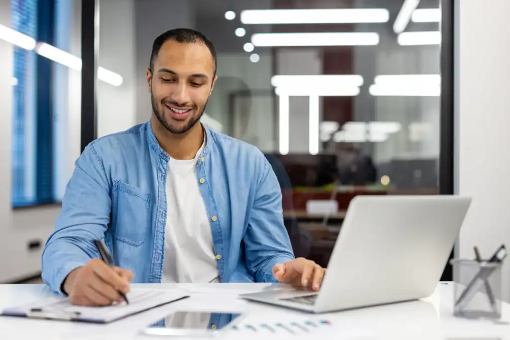 Person reviewing paperwork and taking notes beside a laptop while verifying mental health insurance coverage.