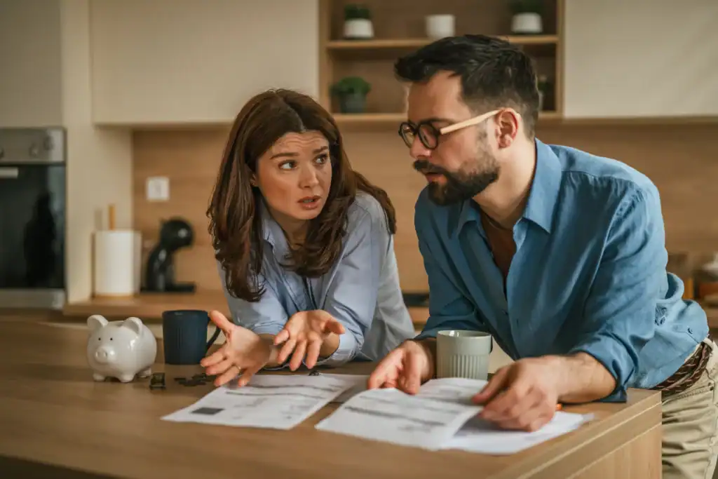 Couple sitting at their kitchen counter discussing medical bills and treatment costs with paperwork spread in front of them