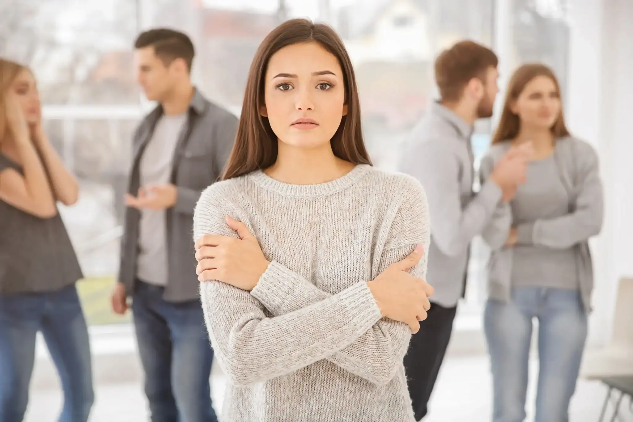 Woman standing alone with arms crossed while others socialize in the background, representing the isolation caused by co-occurring depression and anxiety