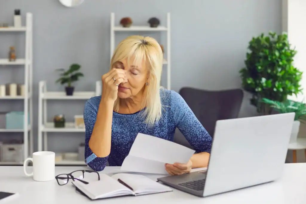 Woman feeling stressed while reading an insurance denial letter at her desk, representing the frustration of a prior authorization denial for mental health treatment