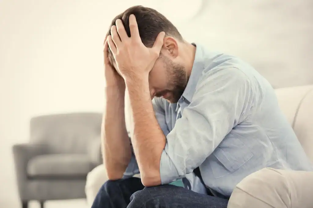 Man sitting alone holding a coffee cup and looking down thoughtfully, reflecting the quiet withdrawal common in adults managing depression and anxiety