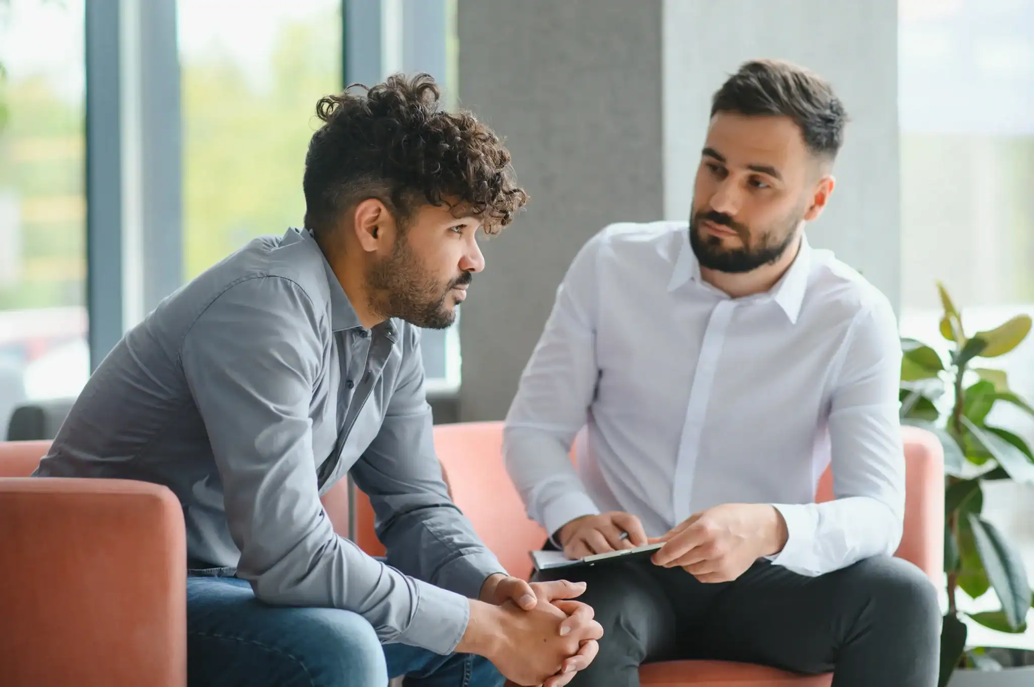 A man in conversation with a male mental health clinician holding a clipboard during a therapy assessment session. A man in conversation with a male mental health clinician holding a clipboard during a therapy assessment session.