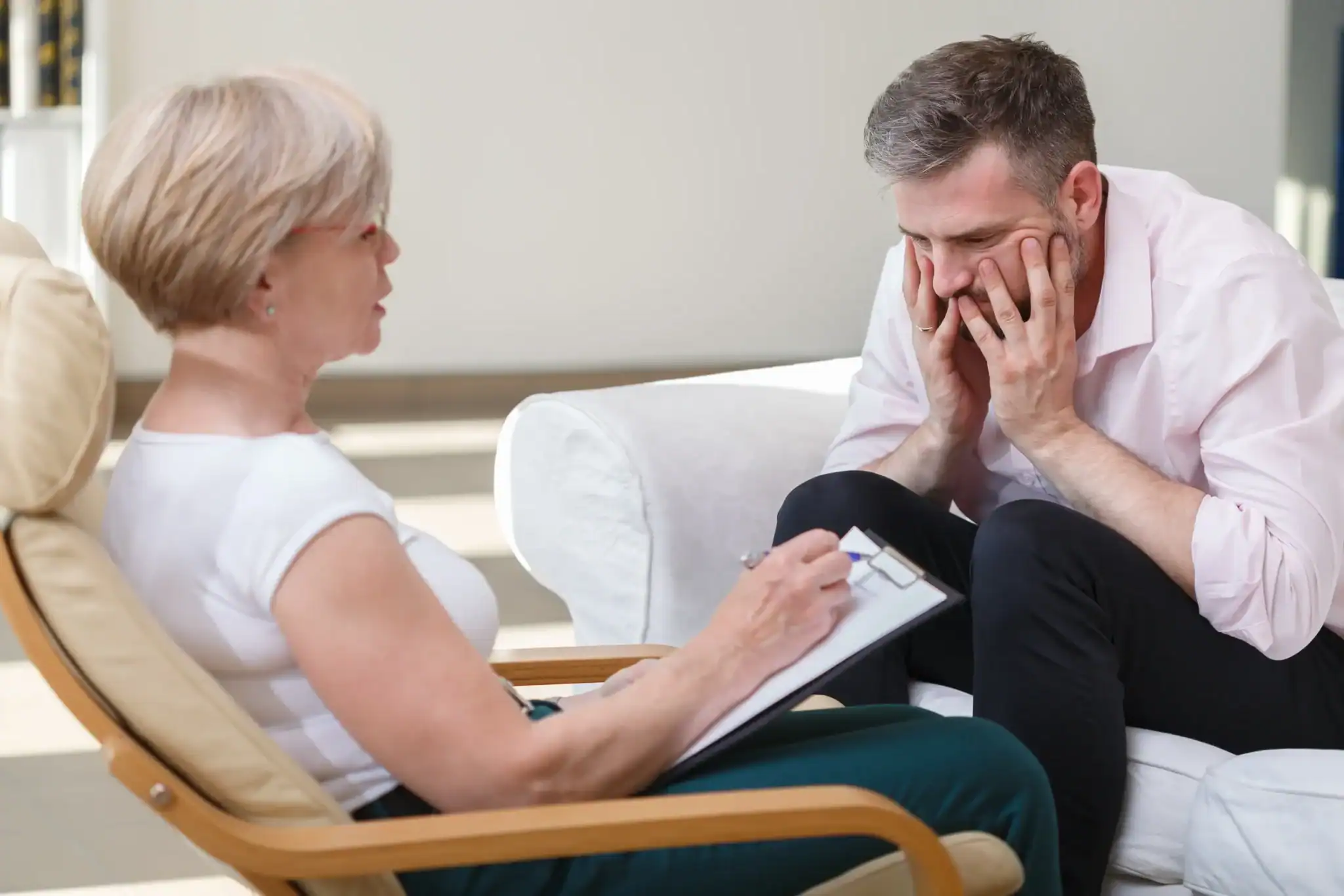 Man with anxiety in a cognitive behavioral therapy session with a clinician taking notes. Man with anxiety in a cognitive behavioral therapy session with a clinician taking notes.